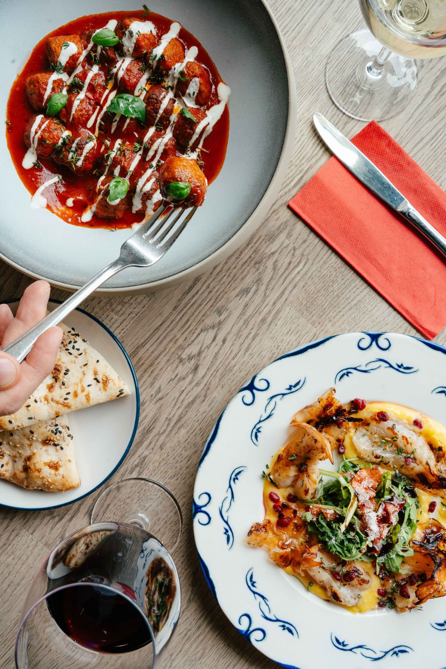 Top view of Italian dishes including meatballs in tomato sauce and pasta with red wine on table.