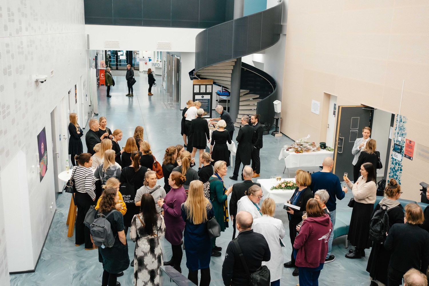 Large group of people gathered in modern building lobby during professional networking reception event.