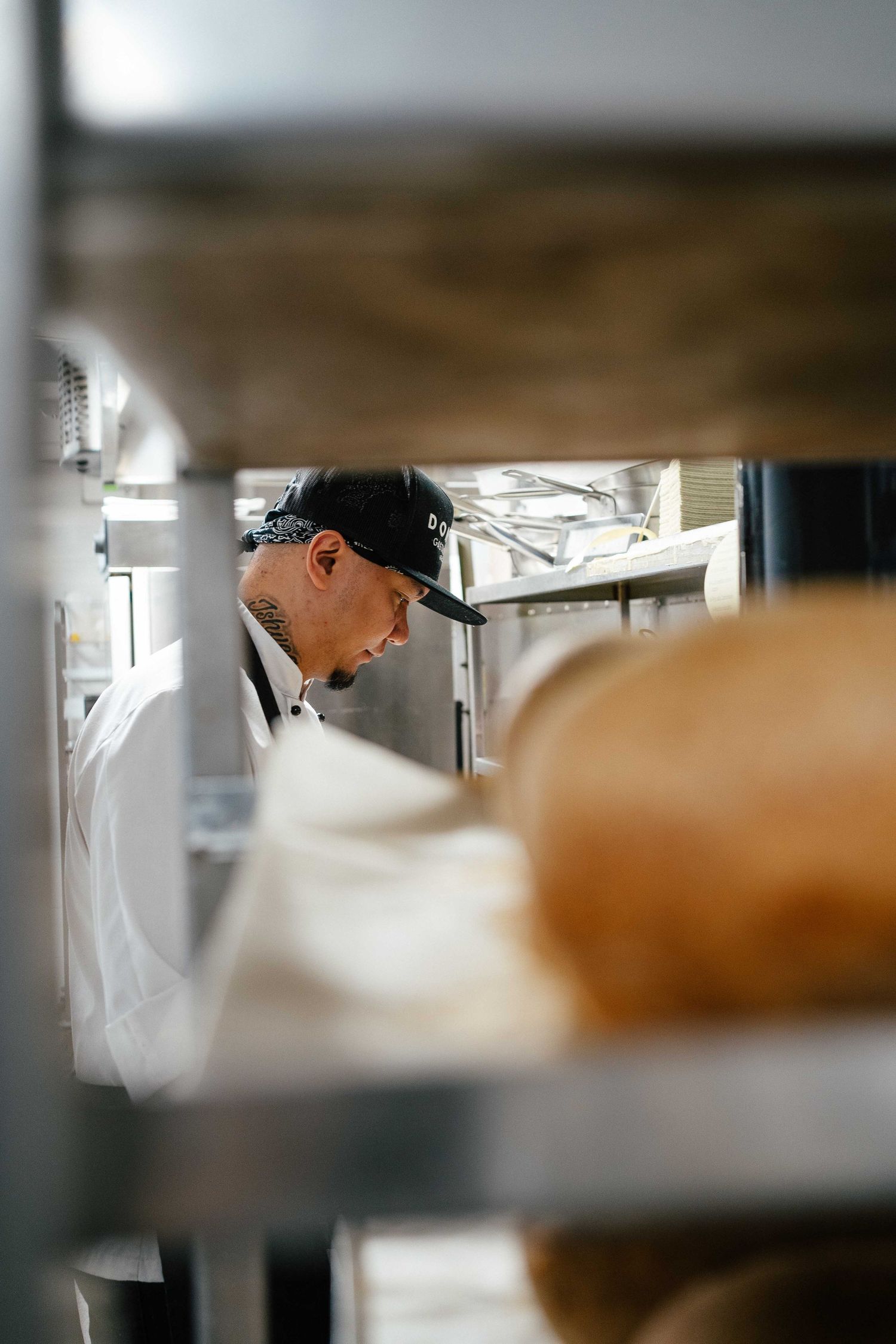 Professional chef working in commercial kitchen, viewed through metal shelving racks.