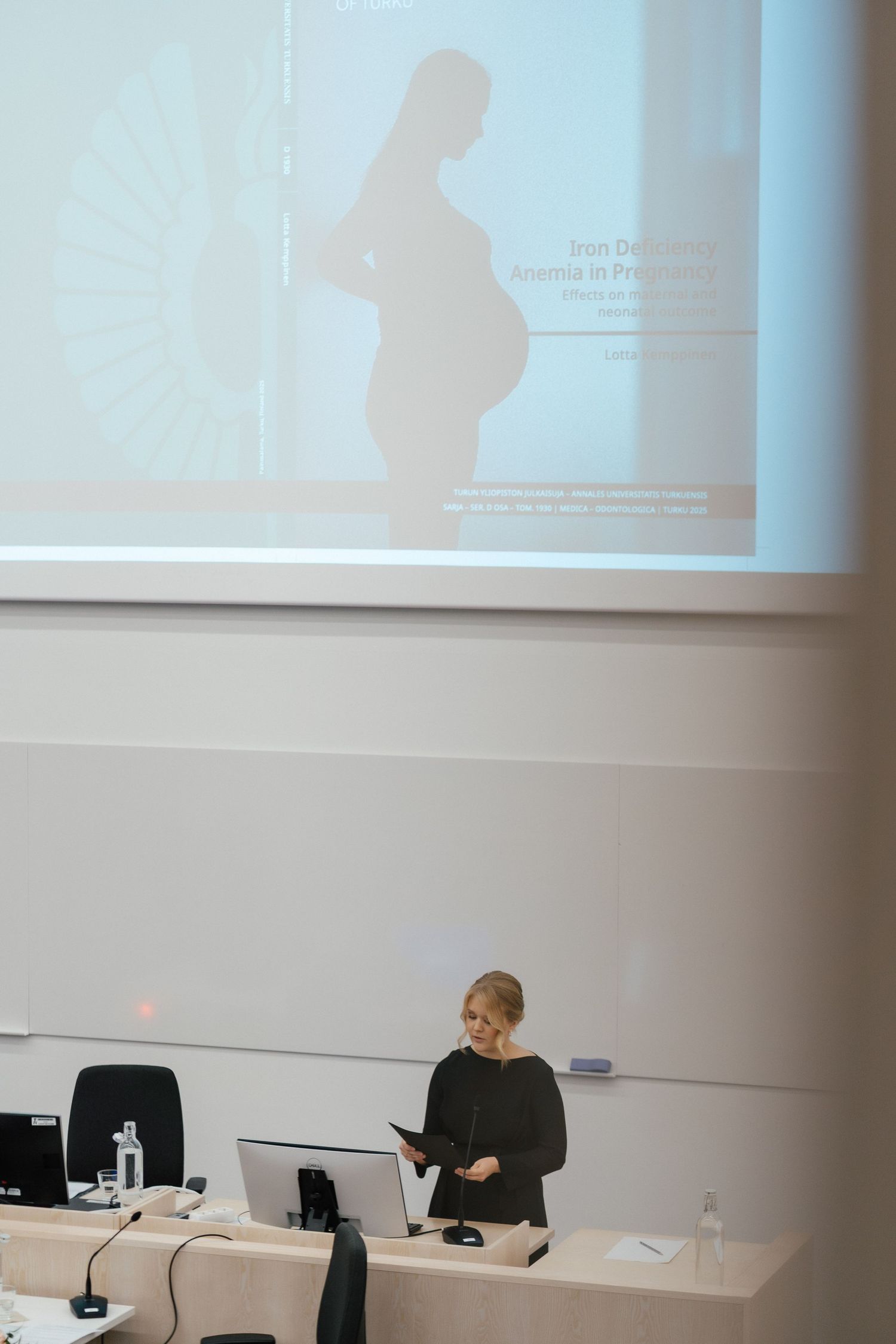 Blonde woman presenting Iron Deficiency Anemia in Pregnancy lecture with projected silhouette slide.
