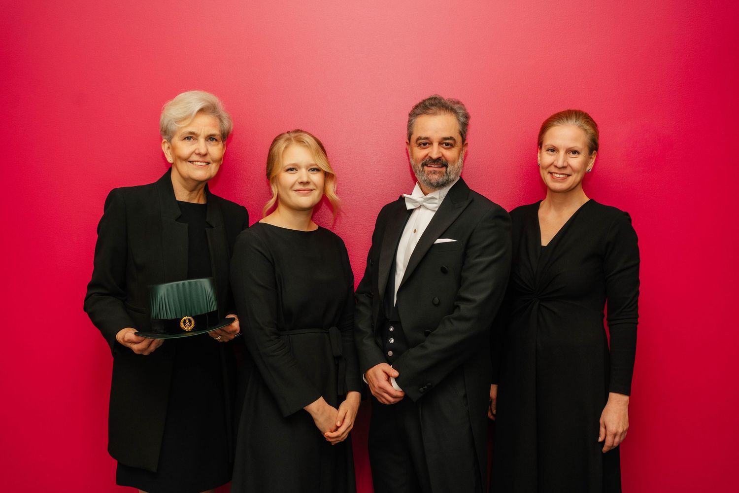 Four elegantly dressed people posing together against red background at formal awards ceremony event.