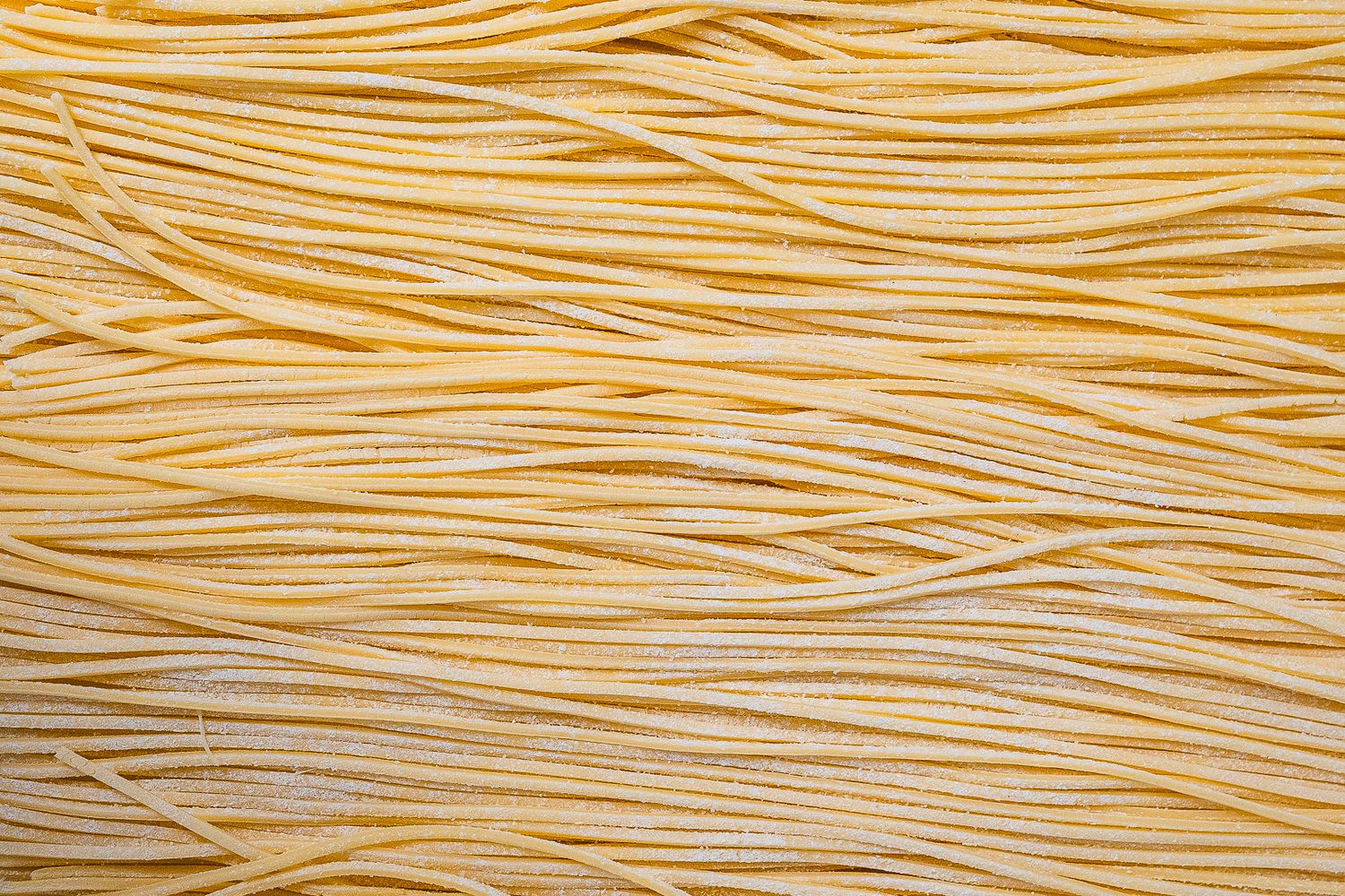Close-up of freshly made thin spaghetti pasta strands laid flat on a floured surface.