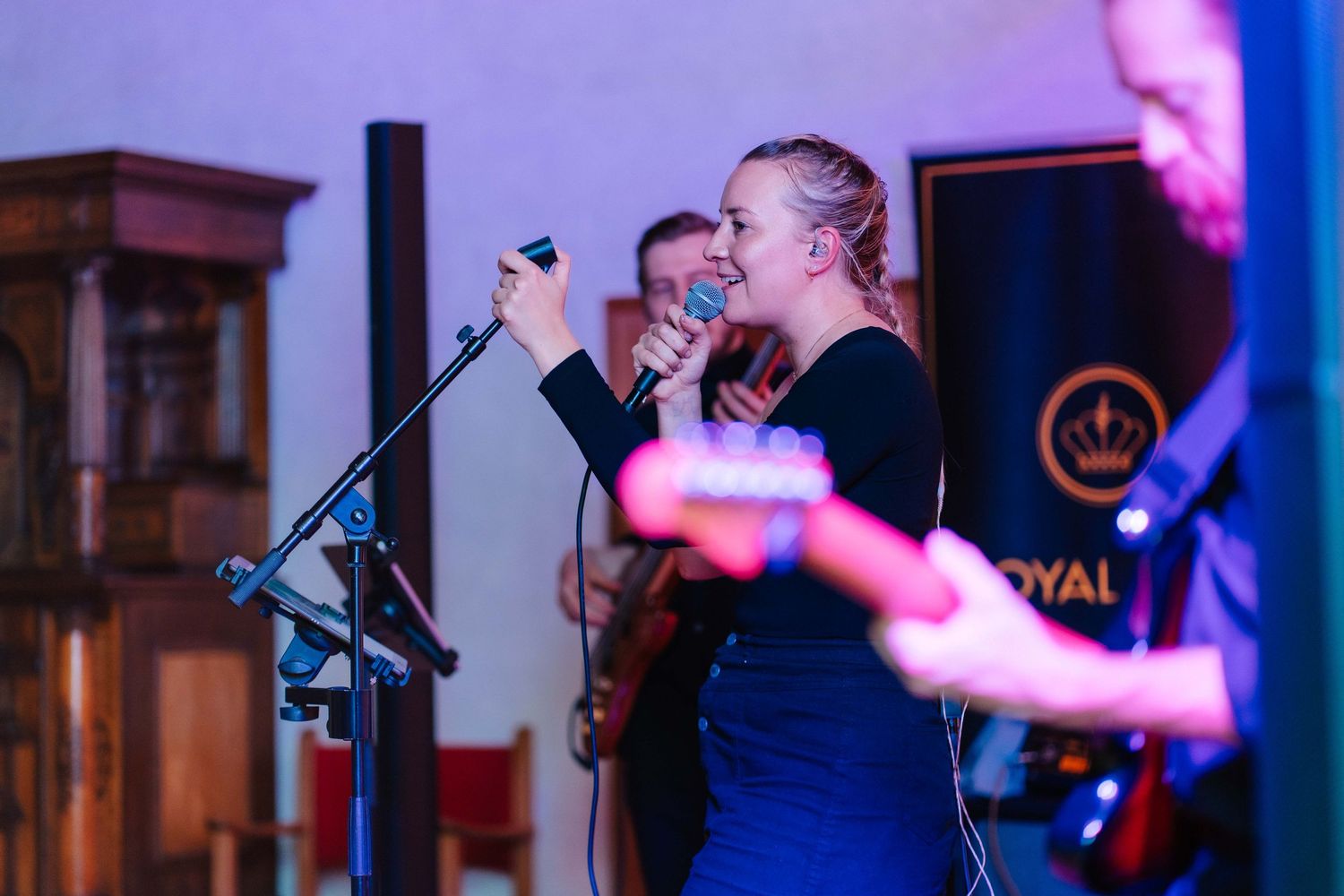 Female vocalist singing into microphone on stage with Royal band banner visible behind her.