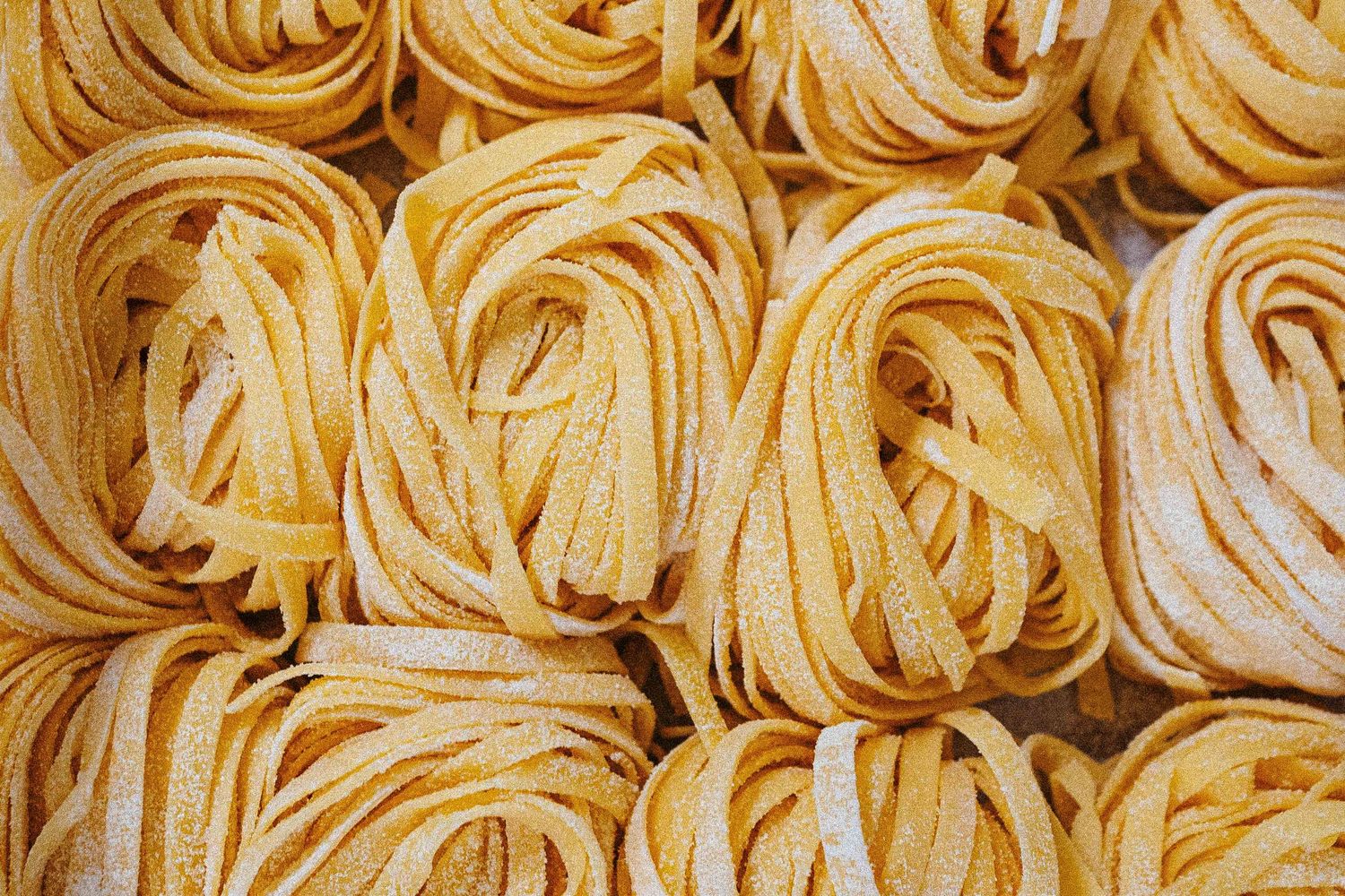 Fresh homemade tagliatelle pasta nests dusted with flour, arranged closely together.