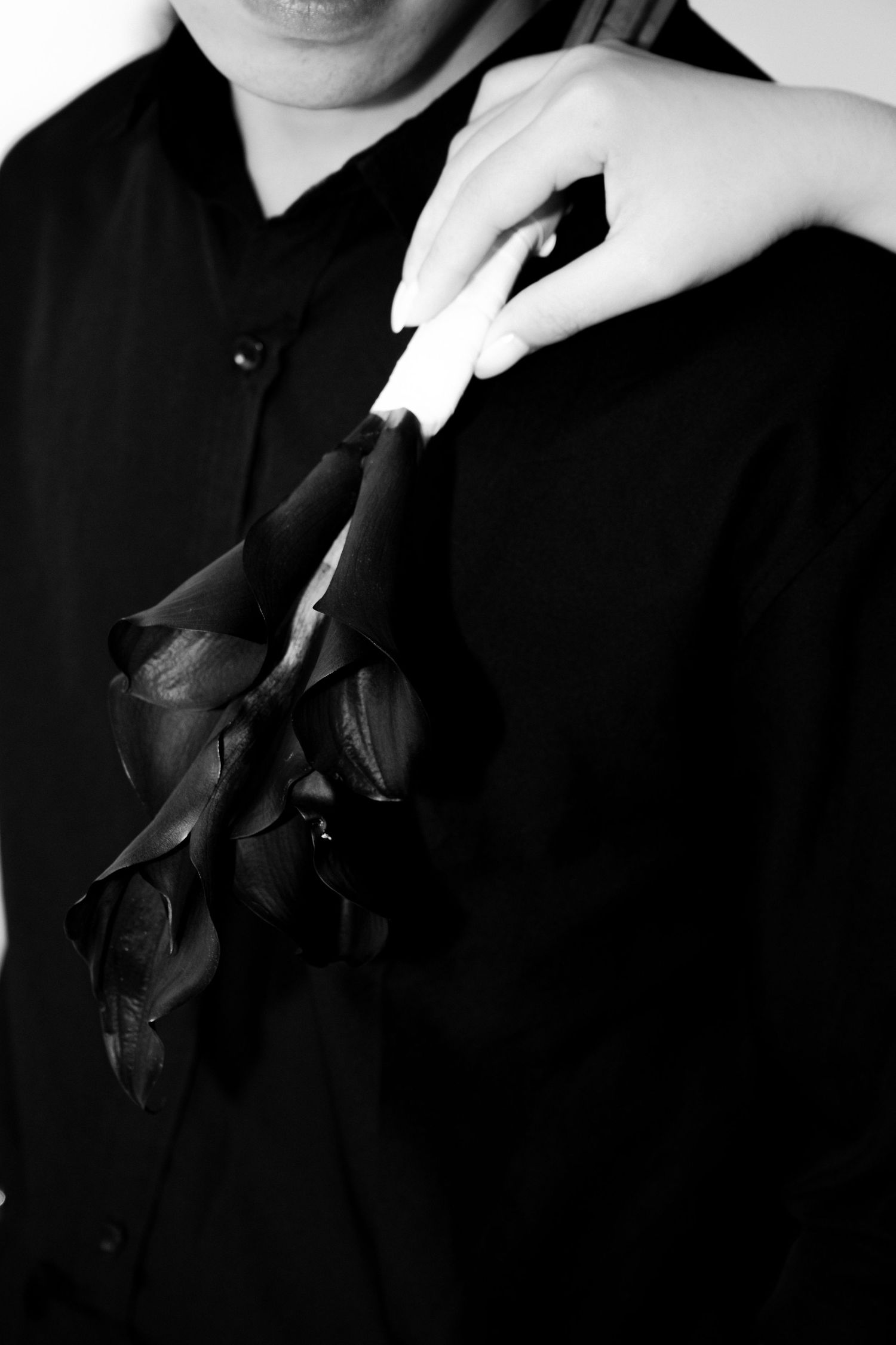 Black and white photo of a person in black holding dark calla lilies with elegant white-tipped nails.
