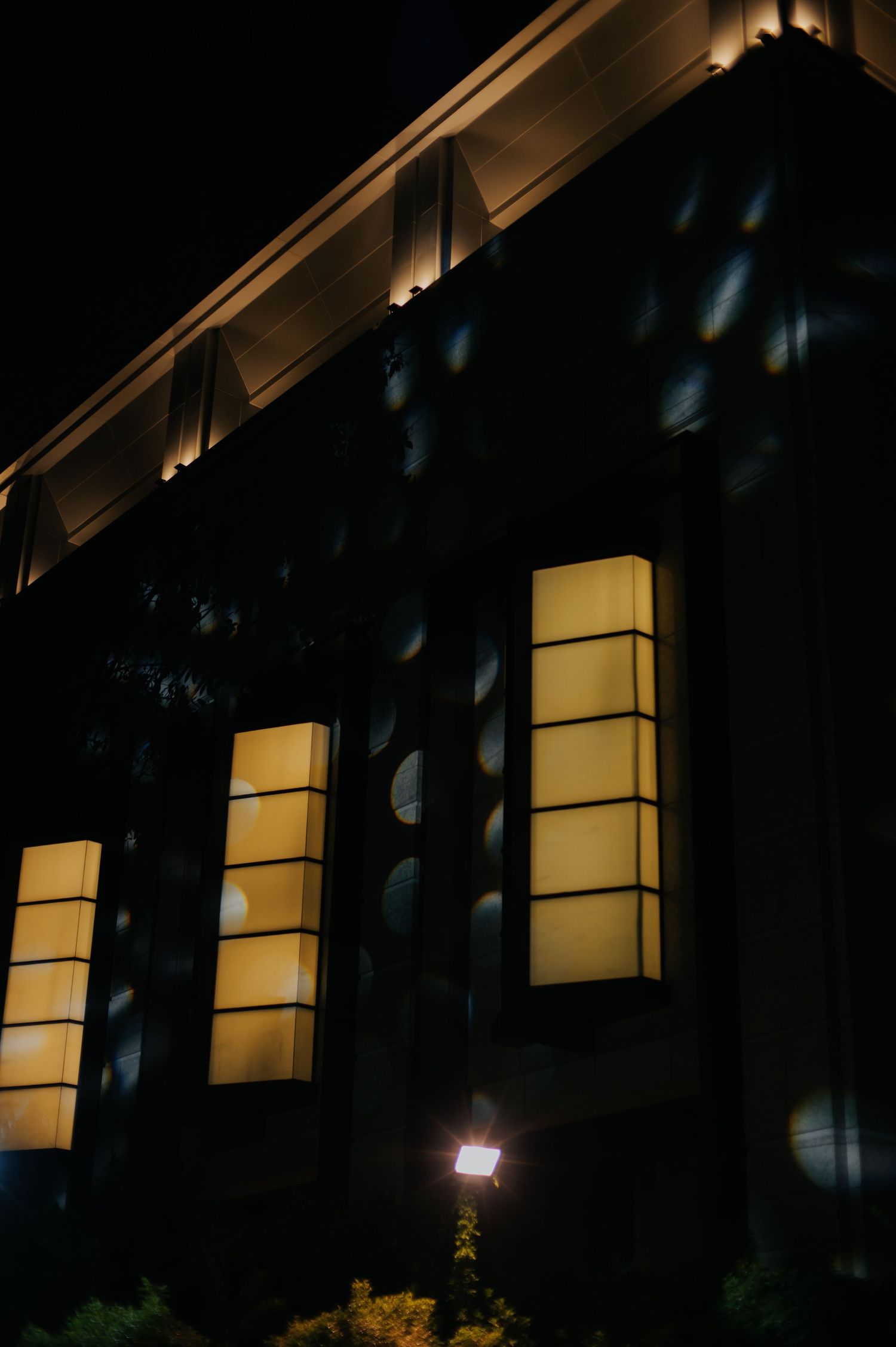 Illuminated building facade at night with glowing rectangular windows and warm accent lighting on cornice.
