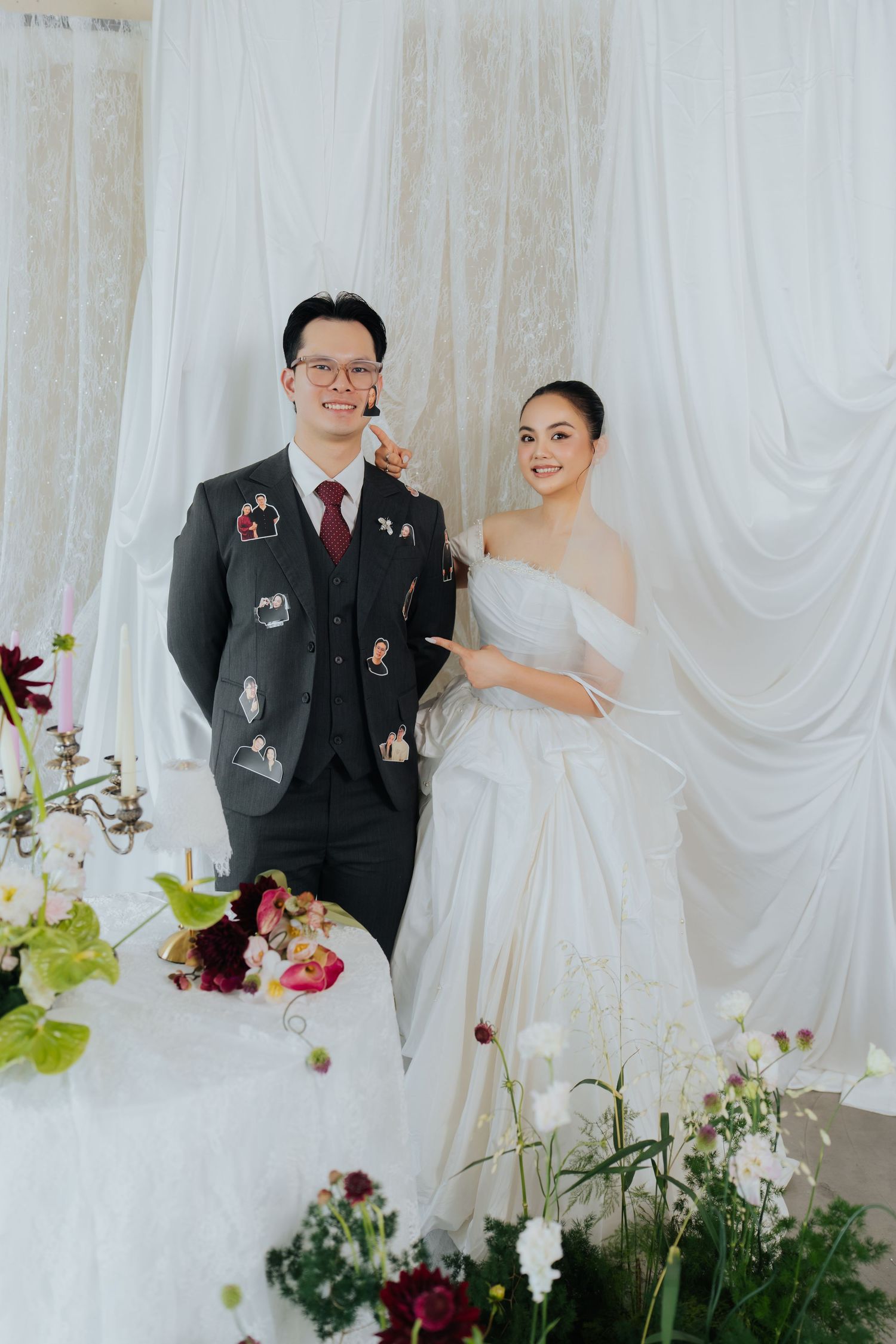 A smiling bride in a white off-shoulder gown and groom in a decorated suit pose together at their elegant wedding reception.