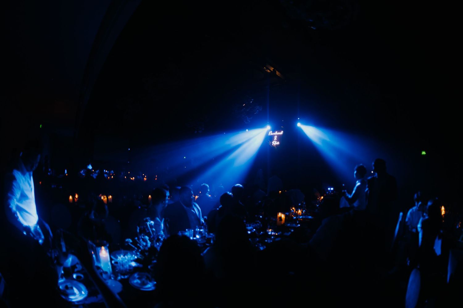 Dark nightclub scene with dramatic blue stage lights illuminating a crowd at tables during an evening event.