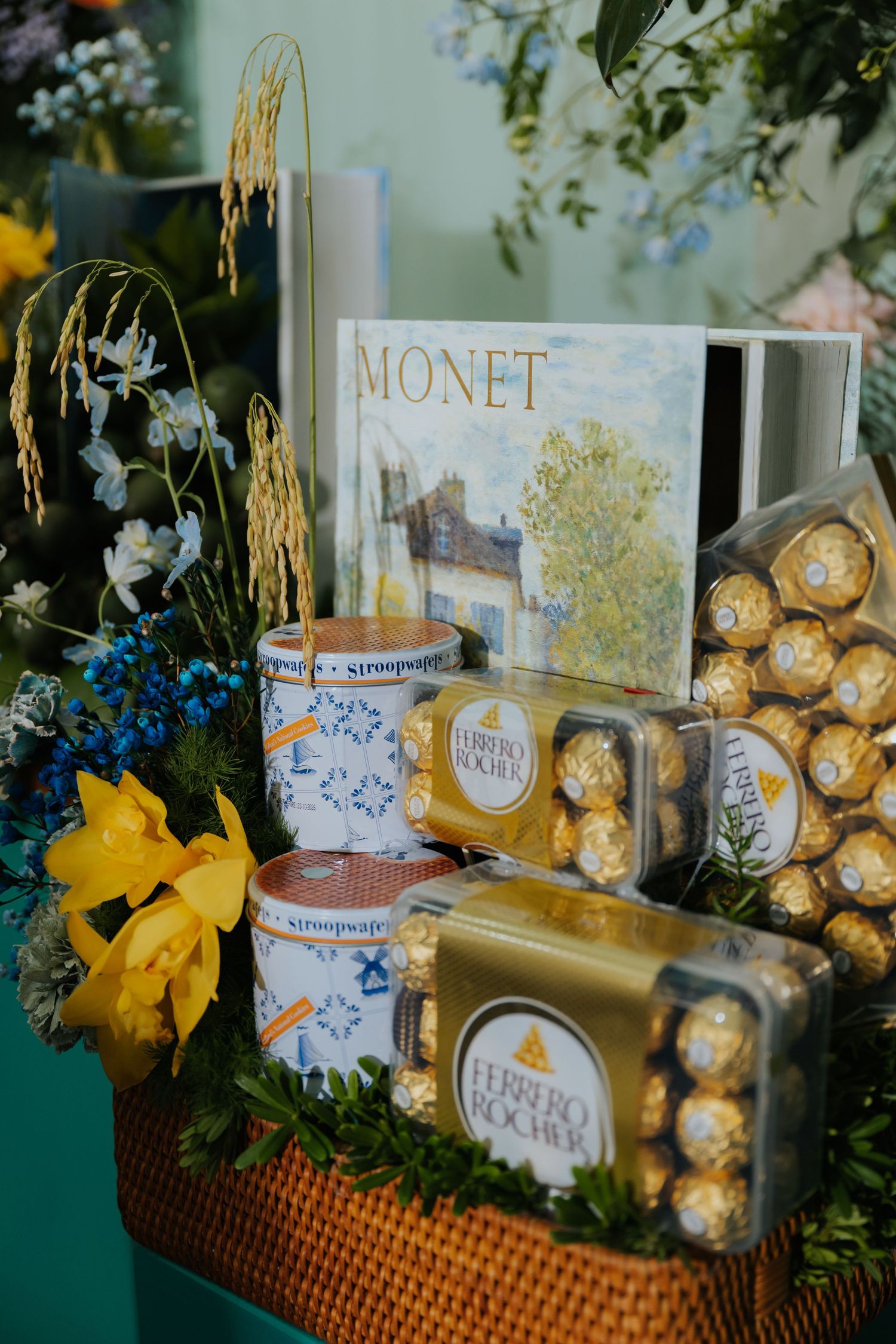 Gift basket with Ferrero Rocher chocolates, Monet art book, stroopwafels, and yellow flowers arranged beautifully.