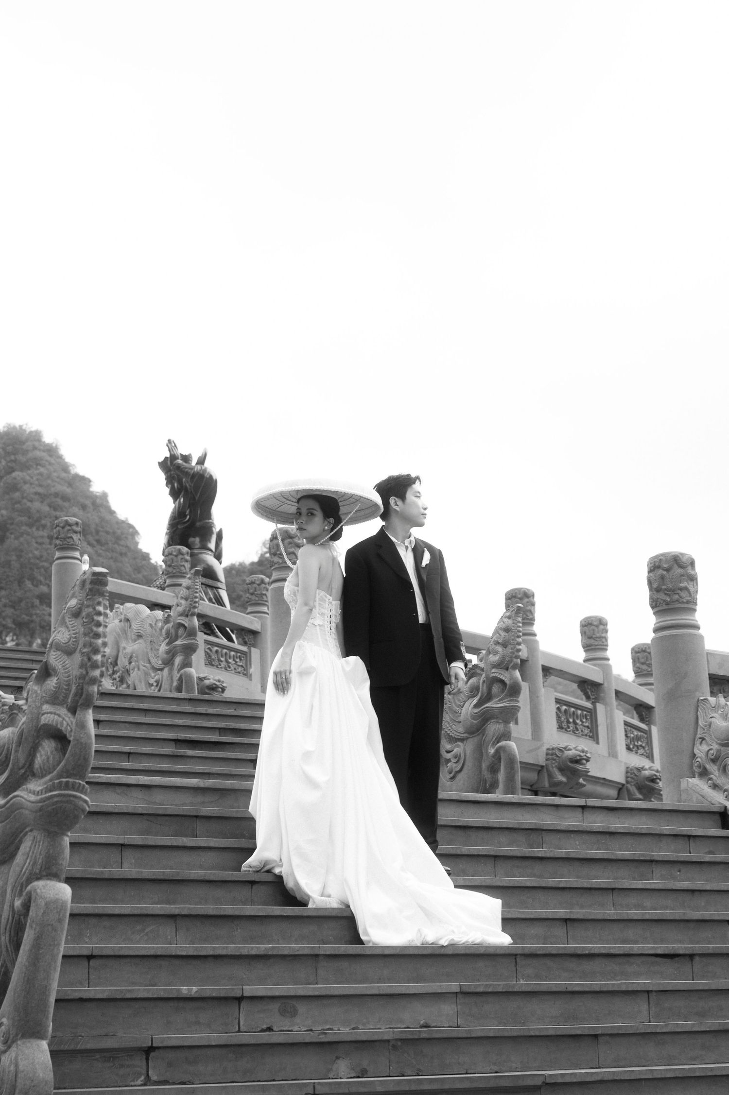 Black and white photo of a bride and groom standing on ornate stone steps at a traditional Asian temple wedding.