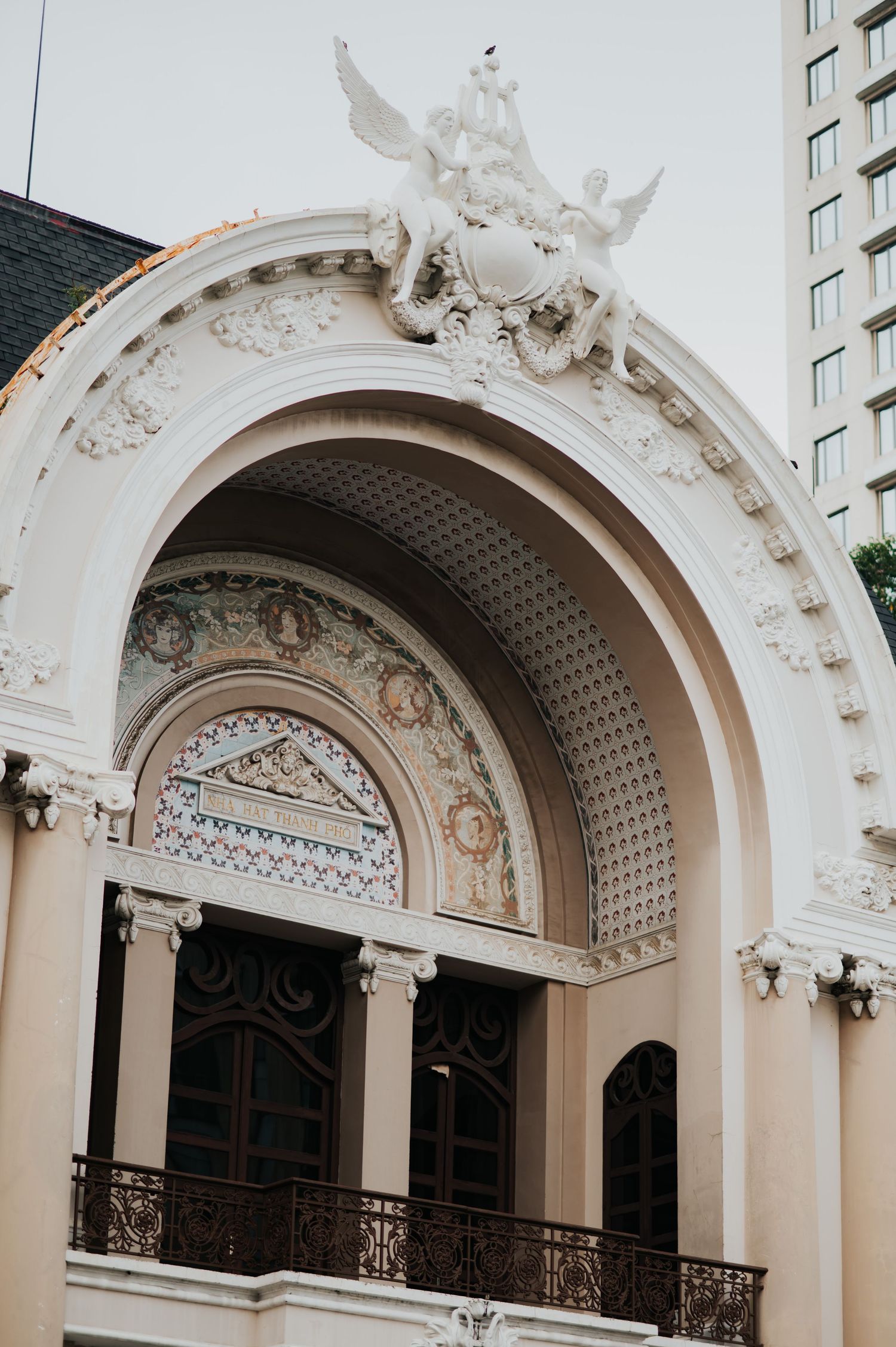 Ornate white neoclassical building facade with arched entrance, decorative sculptures, mosaic details, and wrought iron balcony.