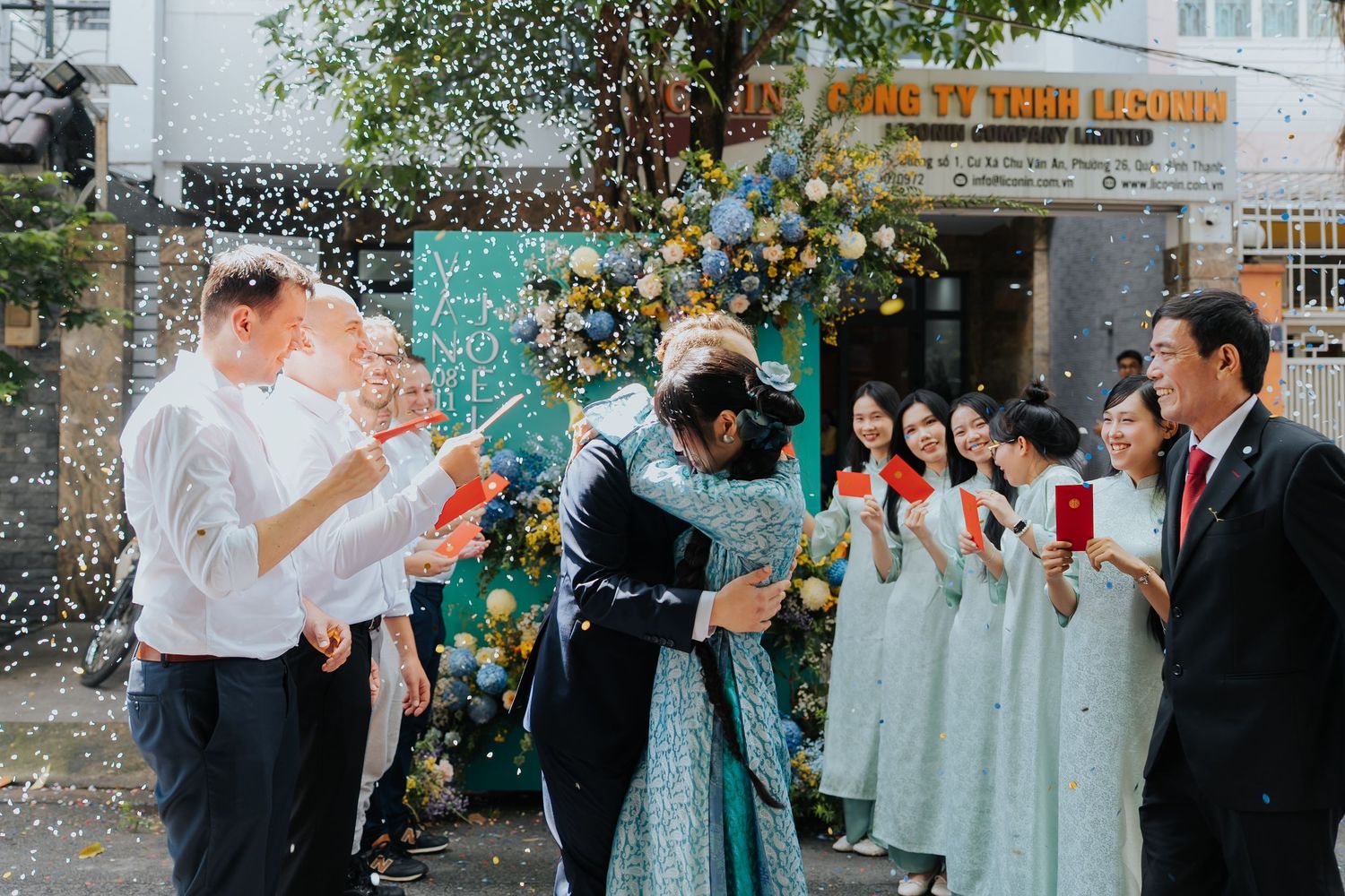 Joyful outdoor wedding ceremony with confetti, bride and groom embracing, bridesmaids in red holding envelopes.