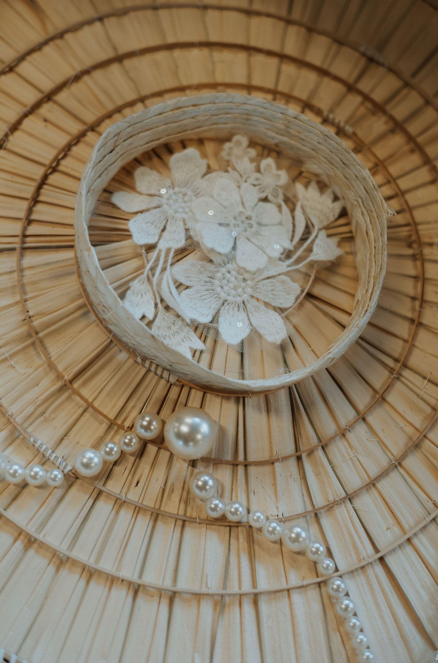 Woven straw hat with white lace flowers and pearl necklace displayed on natural rattan surface.