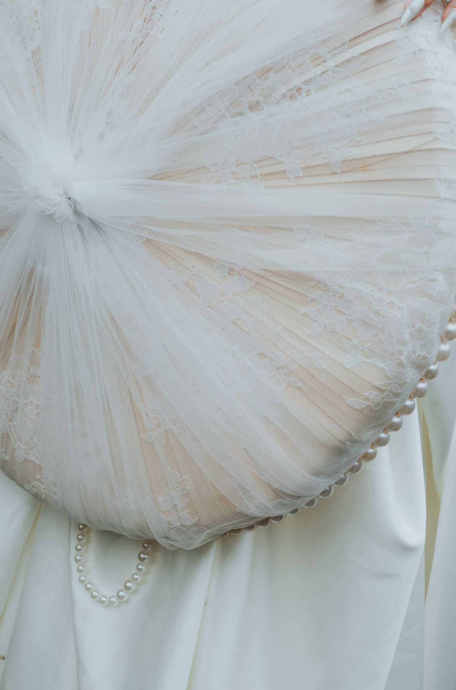 Close-up of an elegant white wedding dress featuring delicate lace tulle fan detail adorned with a pearl bracelet accent.