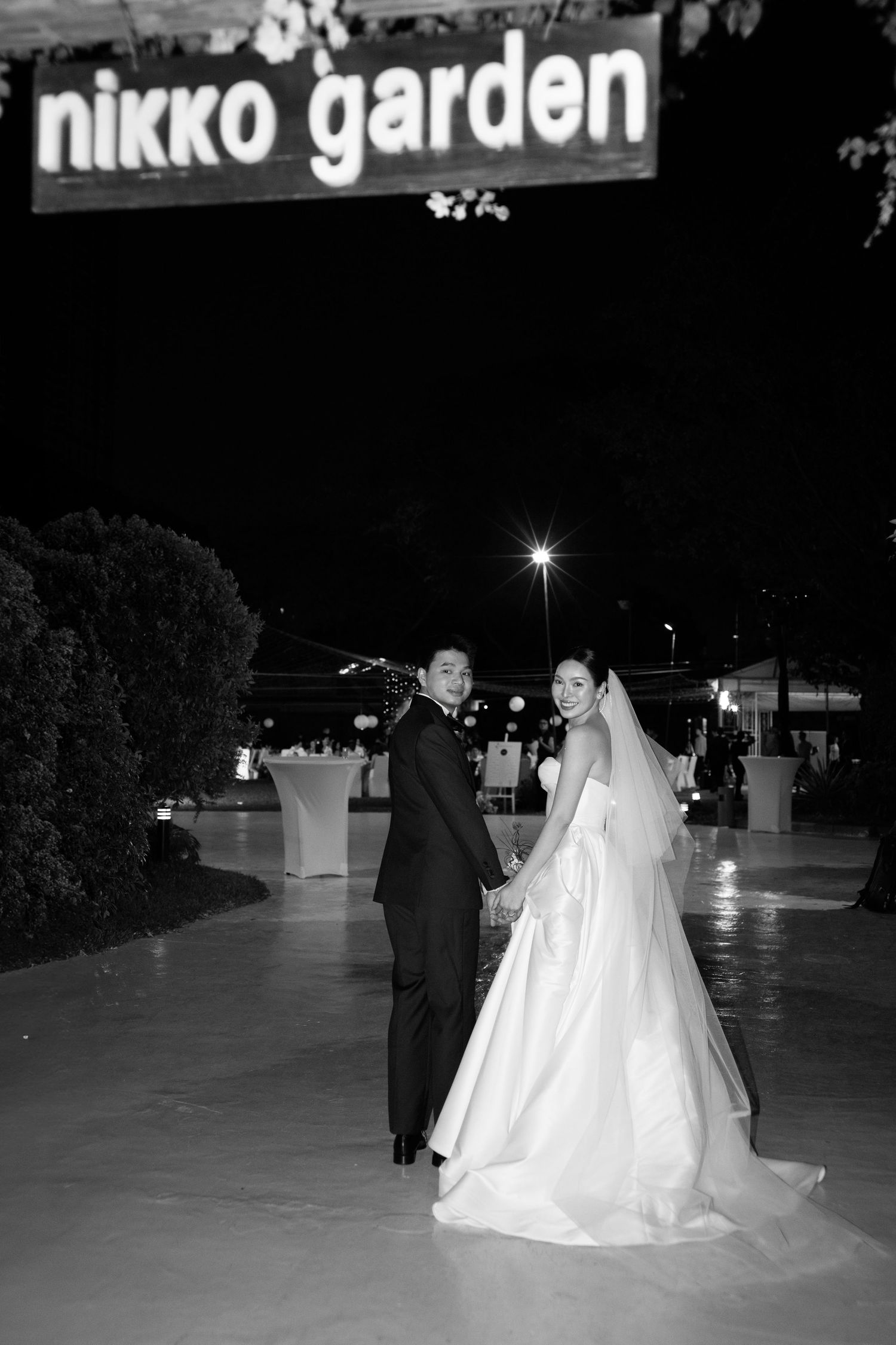 Black and white photo of a bride and groom holding hands at Nikko Garden venue at night.