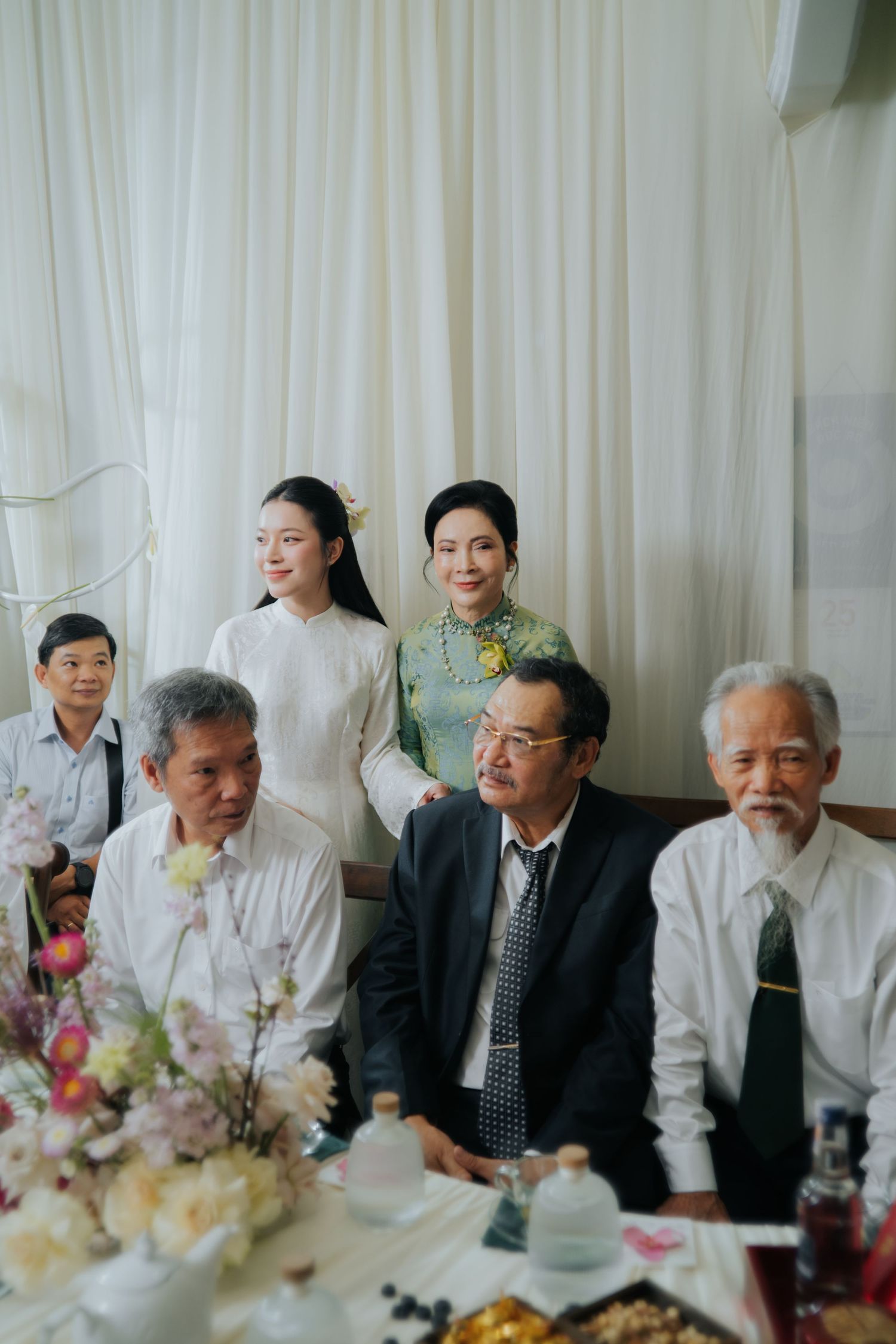 Vietnamese family gathering at a formal event, with women in traditional ao dai and elders seated at a decorated table.