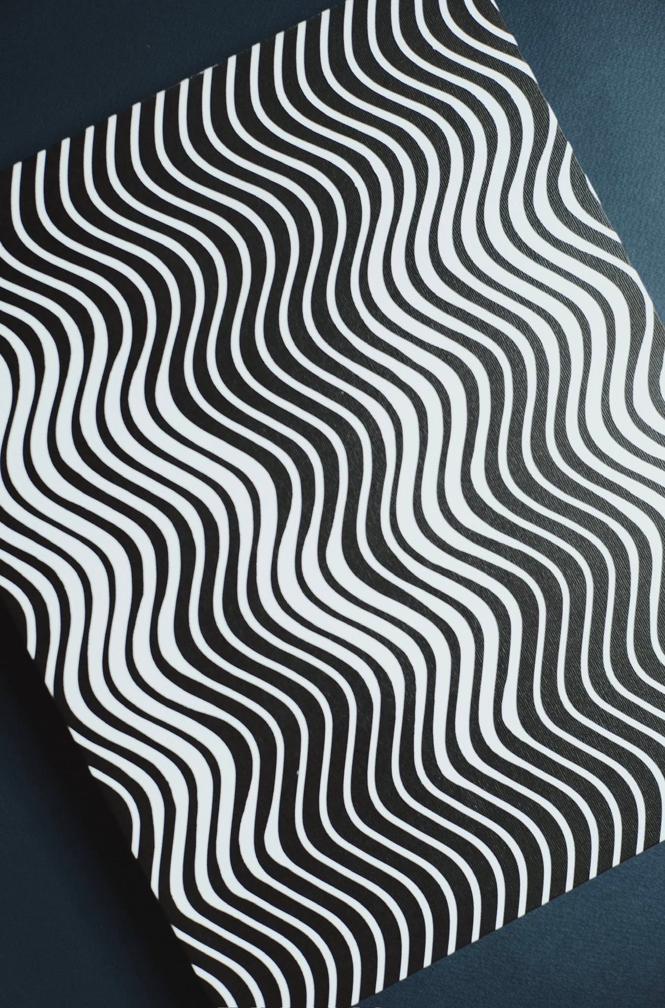Black and white wavy striped pattern creating an optical illusion effect on paper with diagonal undulating lines.