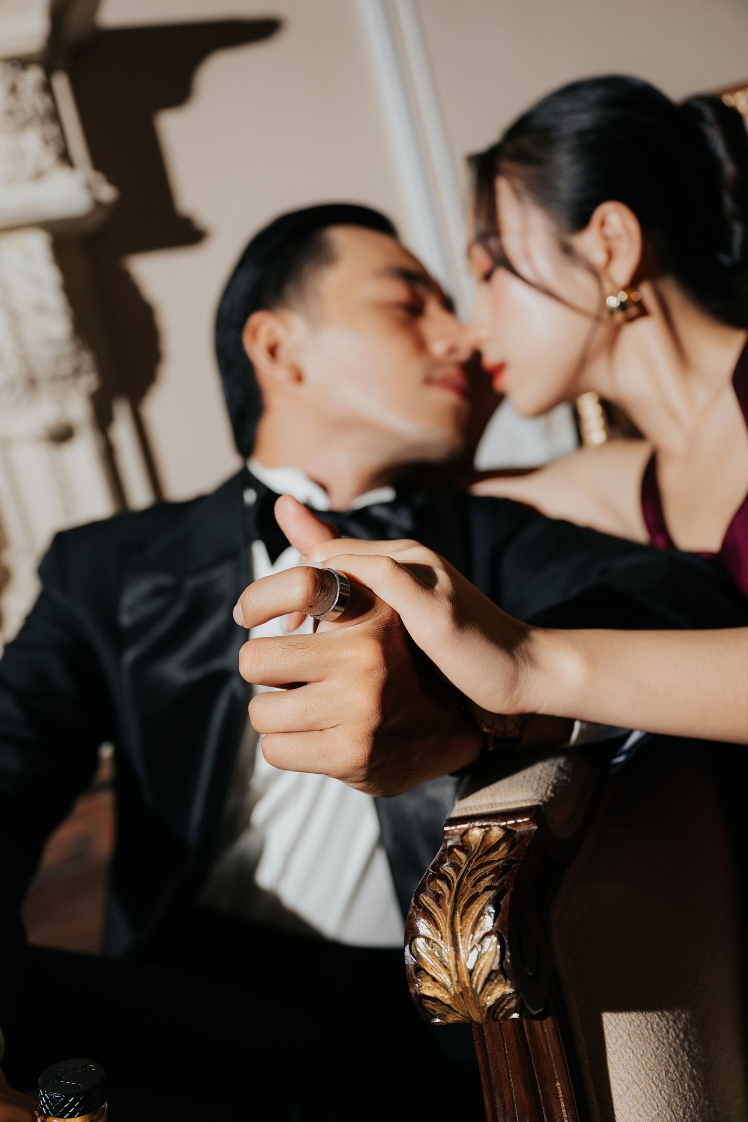 Elegant couple in formal wear sharing a romantic kiss while holding hands in a luxurious interior setting.