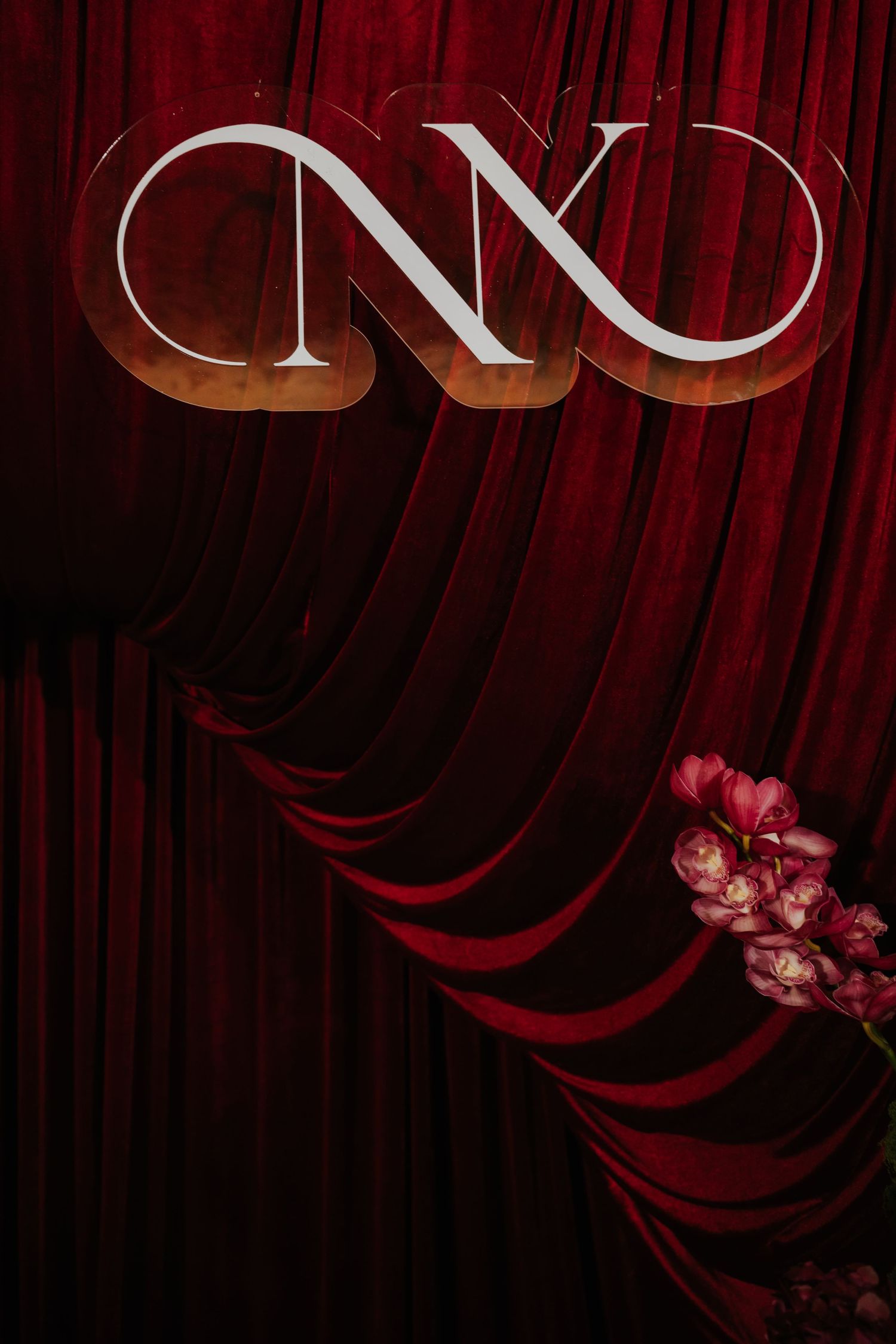 Elegant red velvet curtain backdrop with silver CNX logo and pink orchid flowers in corner.