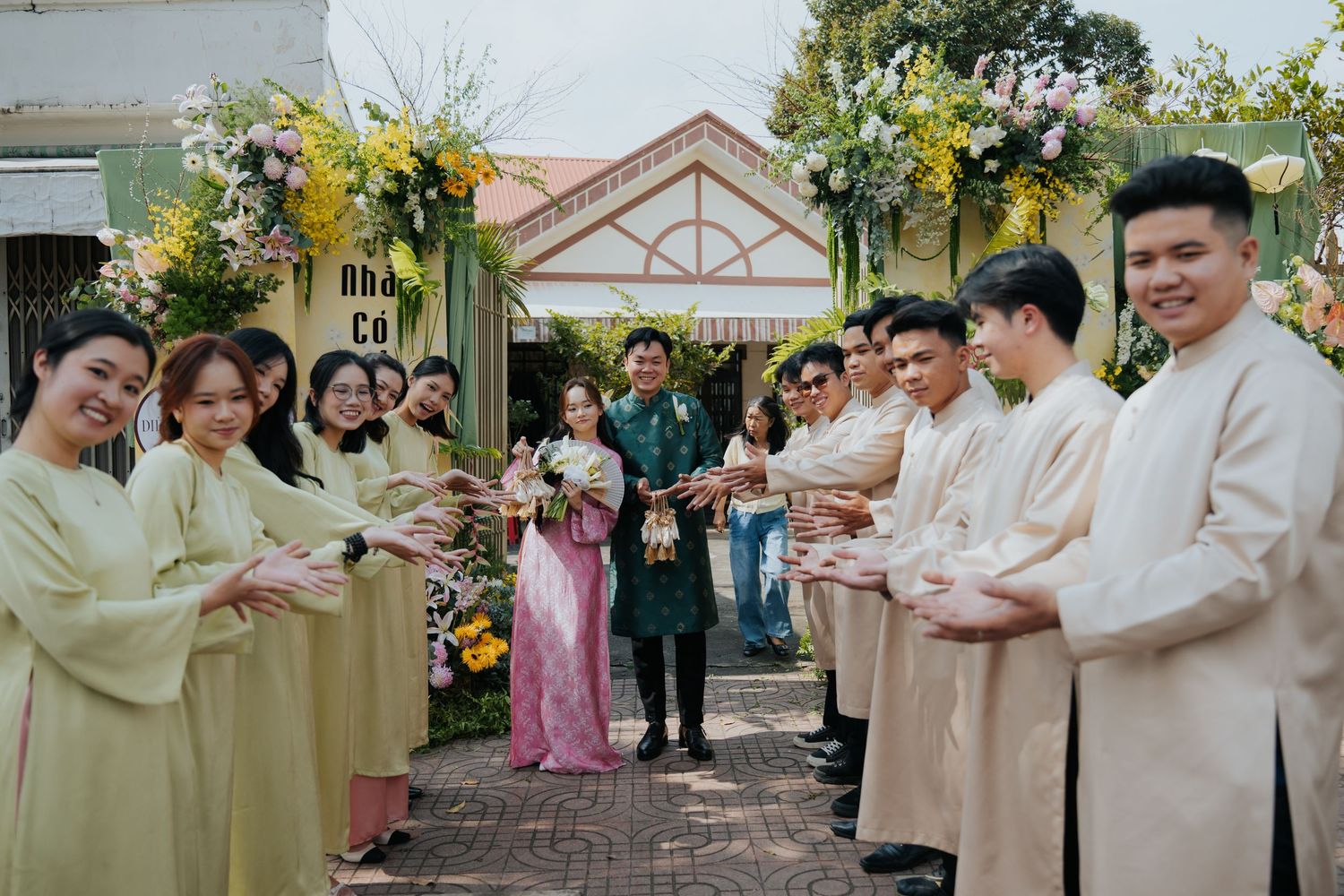 Vietnamese wedding ceremony with bridal party in traditional ao dai attire exchanging gifts at a flower-decorated gate.