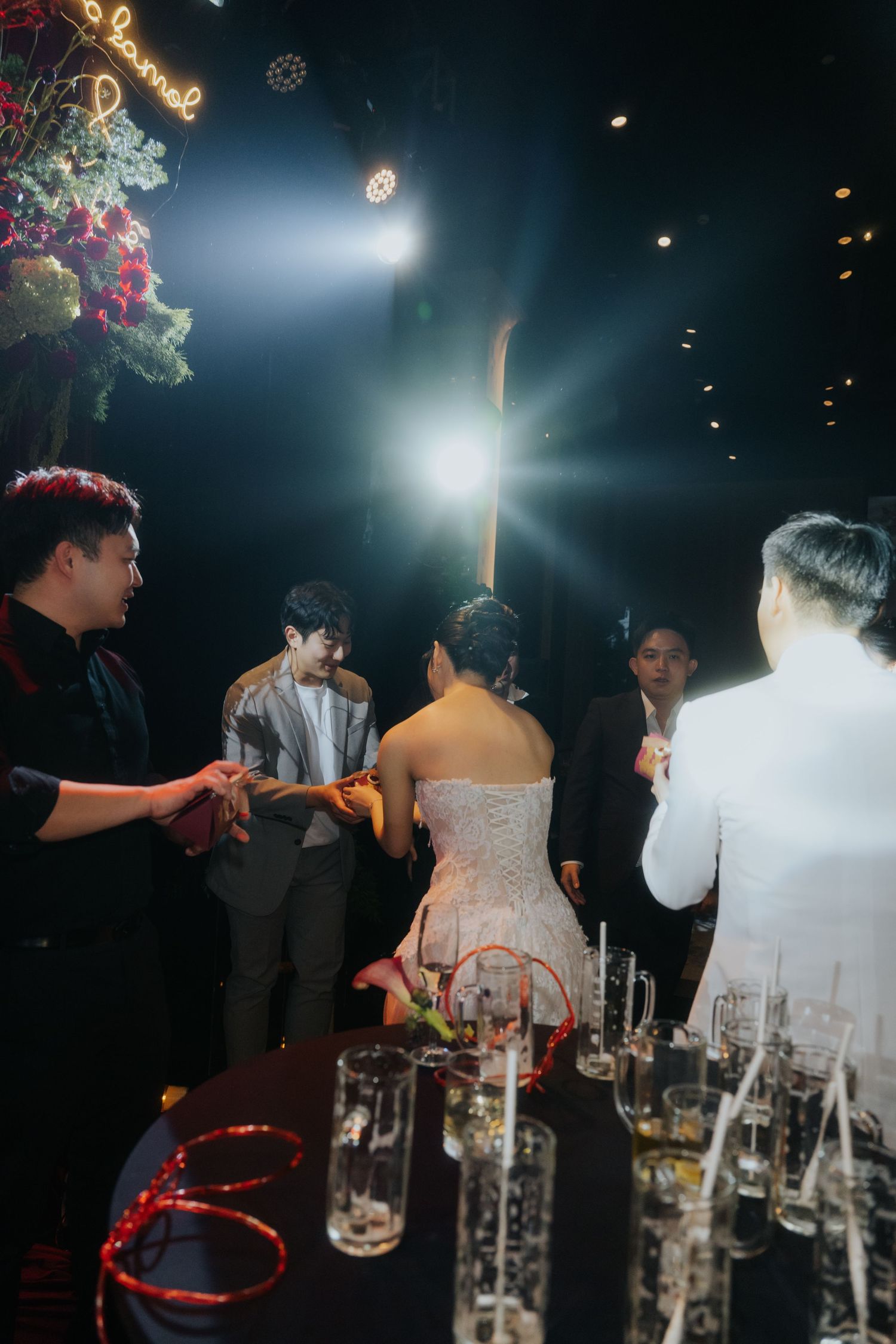 Elegant wedding reception with bride in strapless gown, guests in formal attire, glowing lights, and champagne glasses on table.
