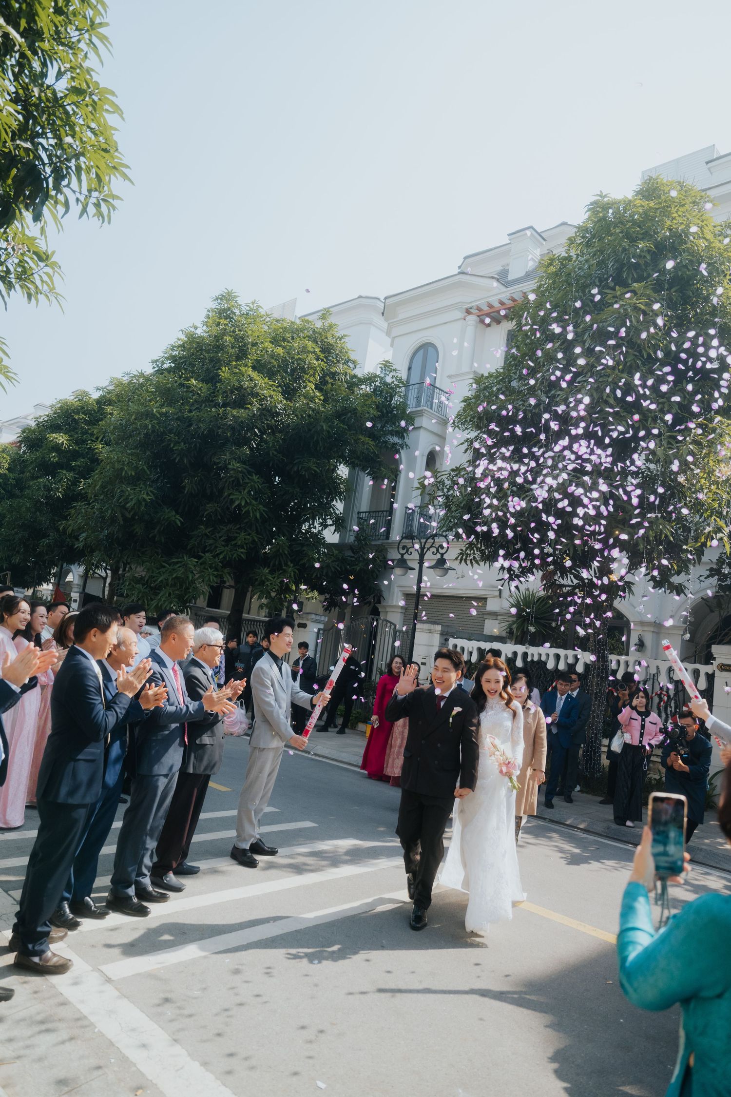 Bride and groom walk through confetti shower as guests celebrate their outdoor wedding ceremony on a sunny day.