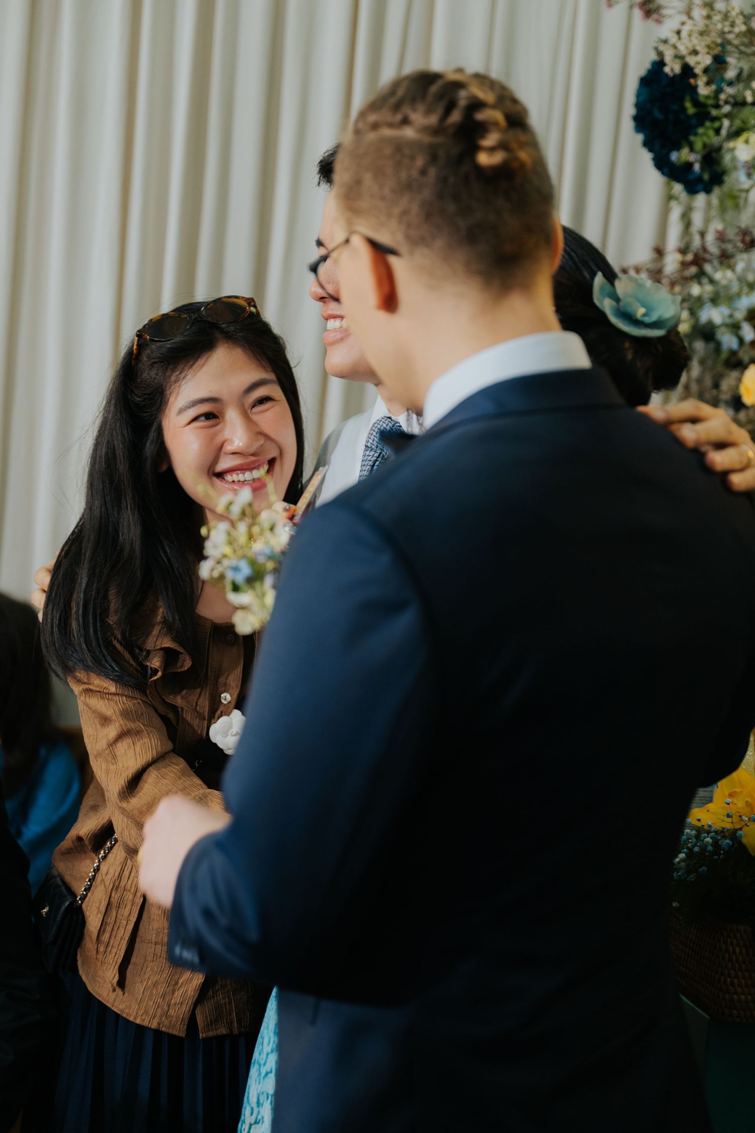 A joyful woman in a brown jacket laughs warmly with guests at an elegant wedding reception.