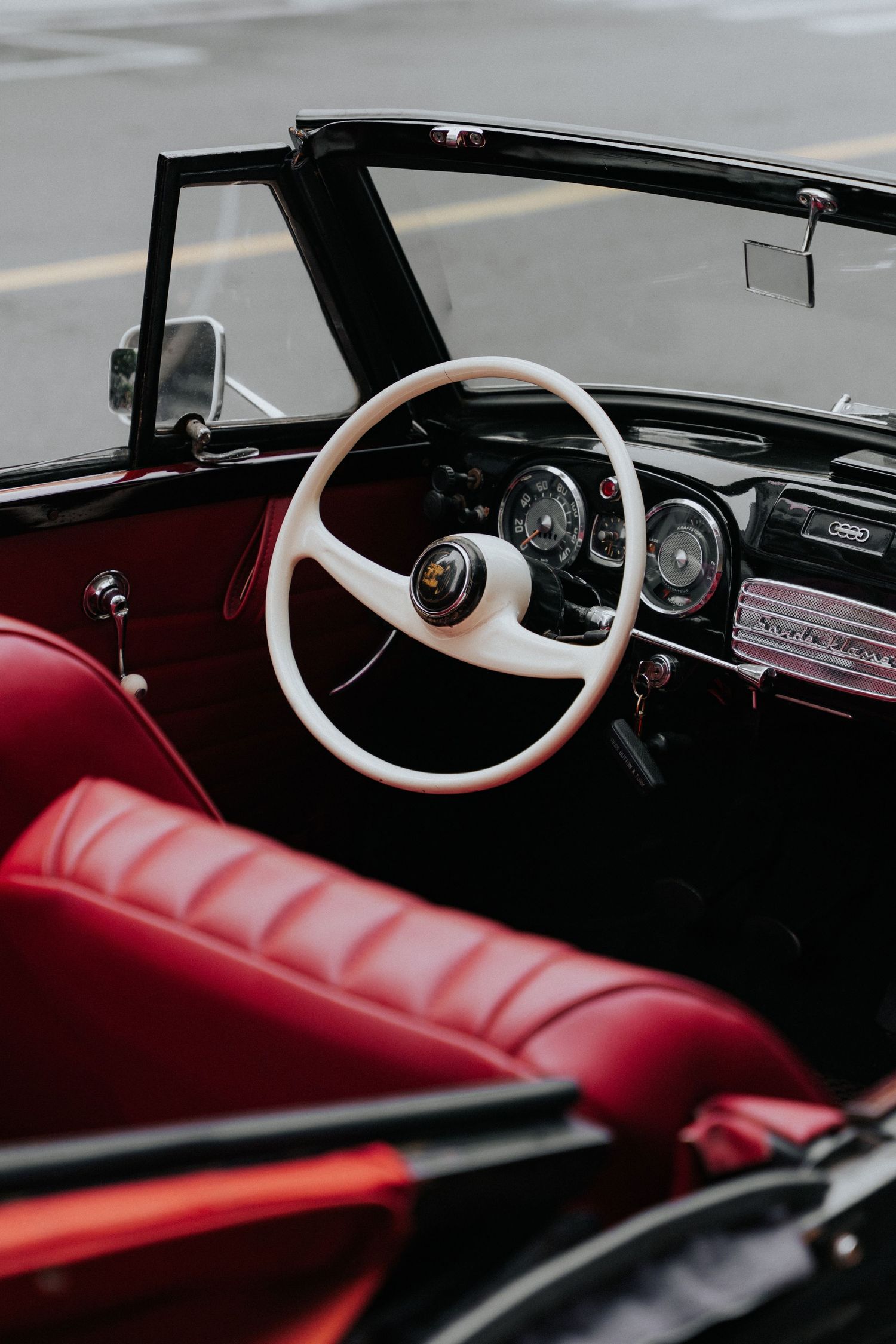 Vintage convertible car interior with white steering wheel and red leather seats.