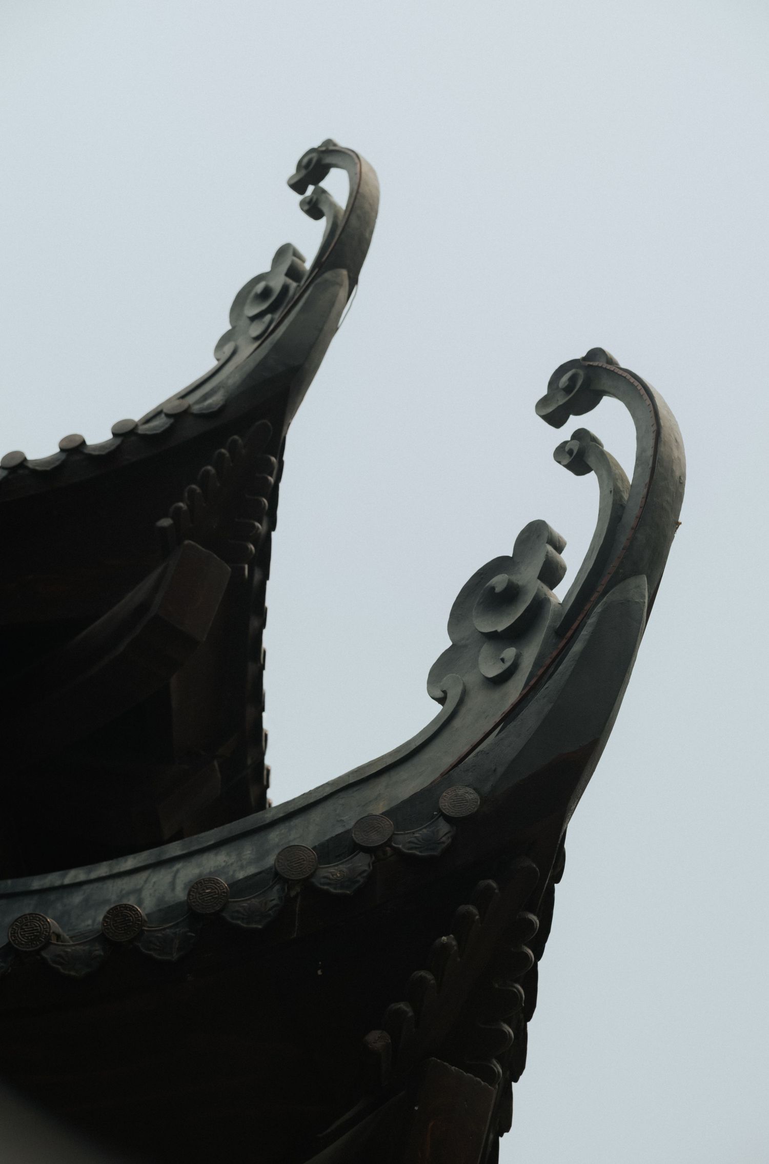 Close-up of ornate dark curved eaves tips of a traditional Chinese temple roof against a gray sky.