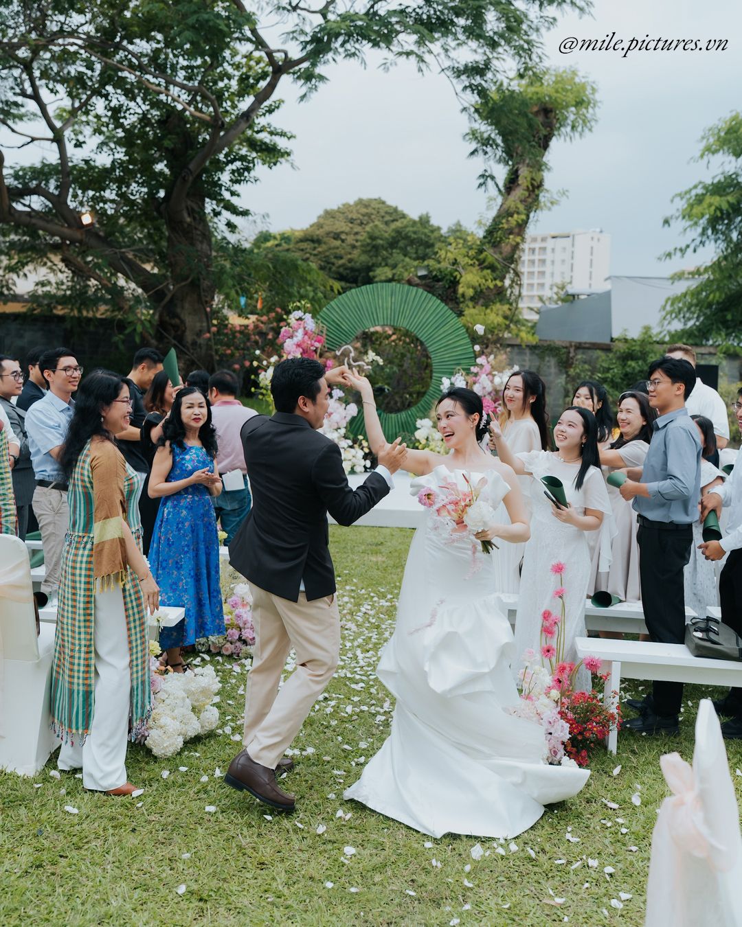 Bride and groom dancing outdoors at a garden wedding ceremony surrounded by guests holding flowers.