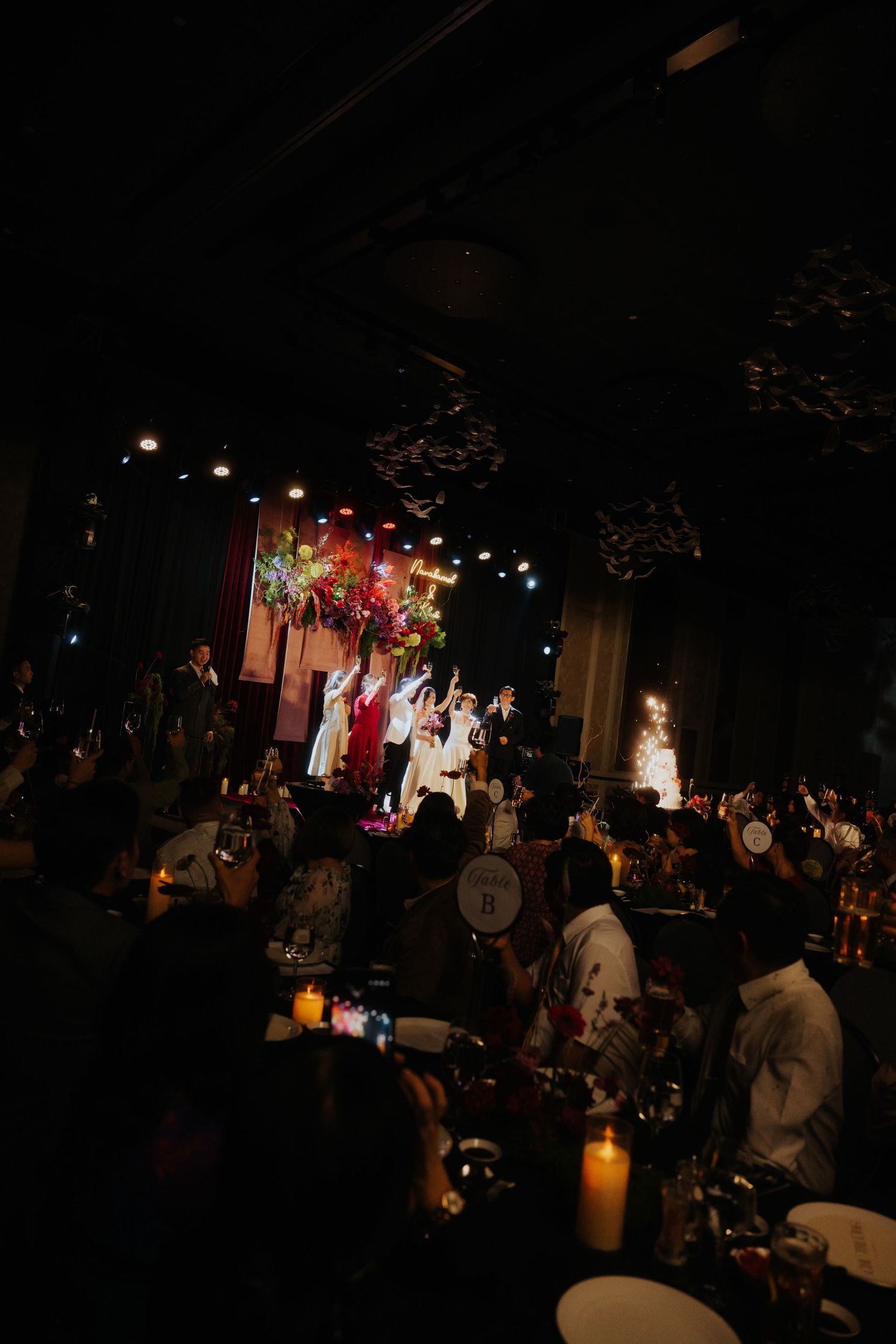 Guests seated at candlelit tables watch performers on a colorful stage during an elegant evening gala event.