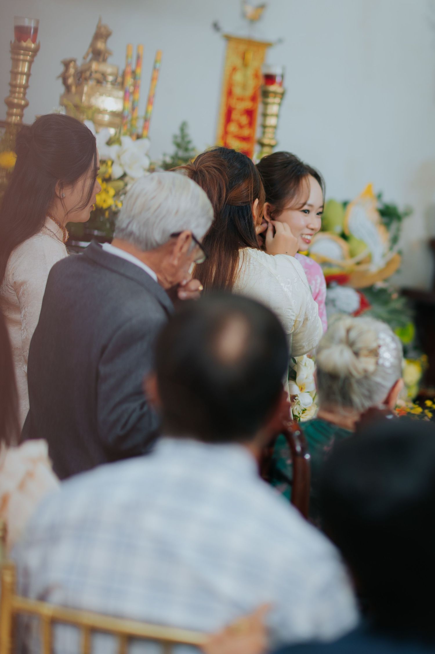 Guests gather at a Vietnamese ceremony with floral arrangements and golden altar decorations in the background.
