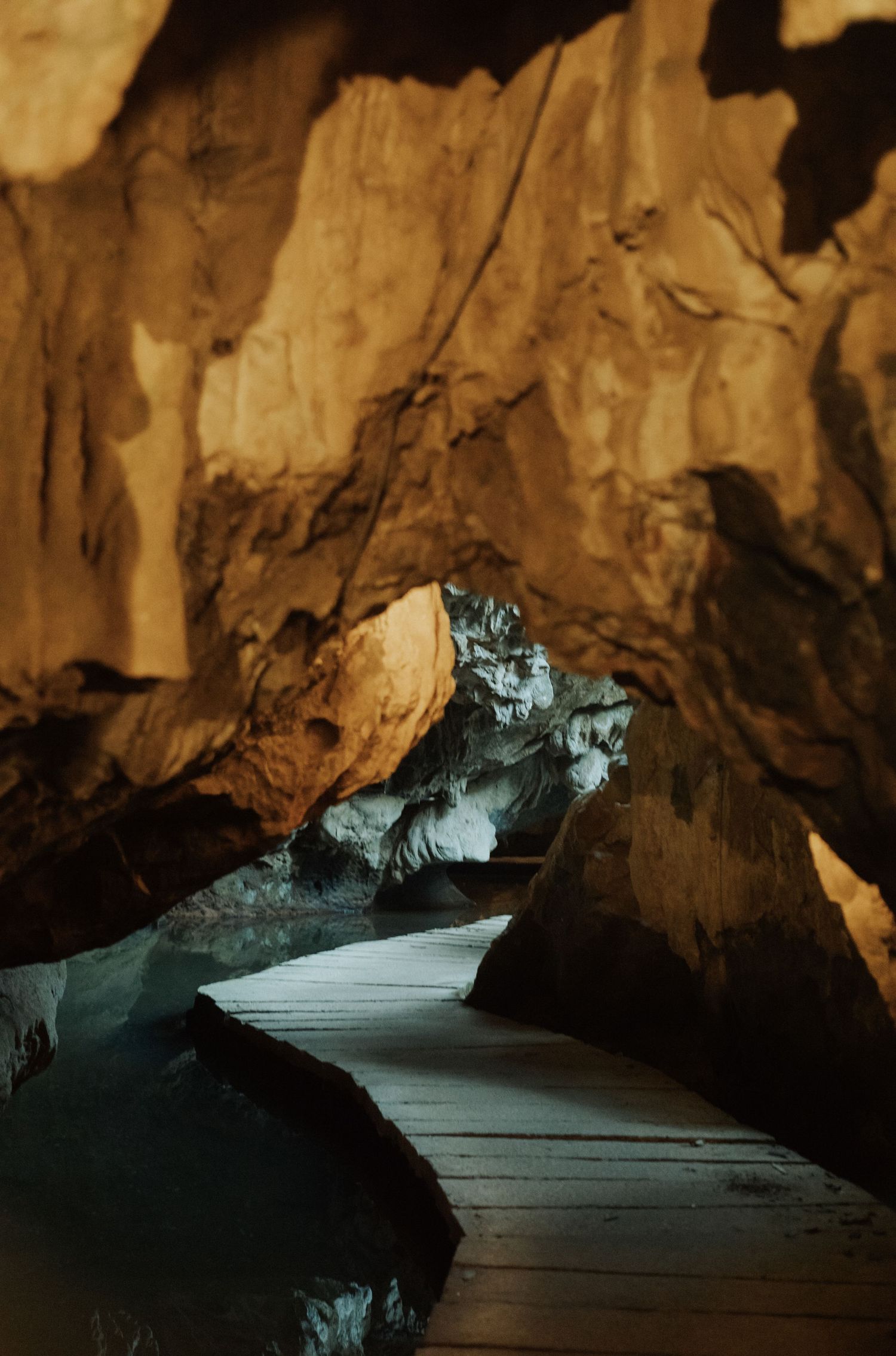 A wooden boardwalk path leads through a dramatic illuminated cave with golden rock formations.