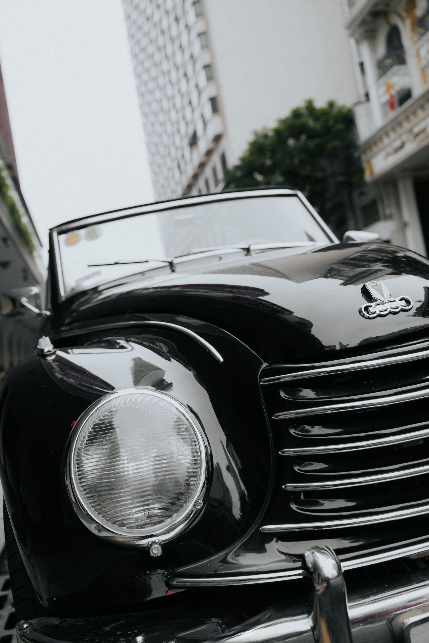 Vintage black classic convertible car with chrome grille and round headlights parked on urban street.
