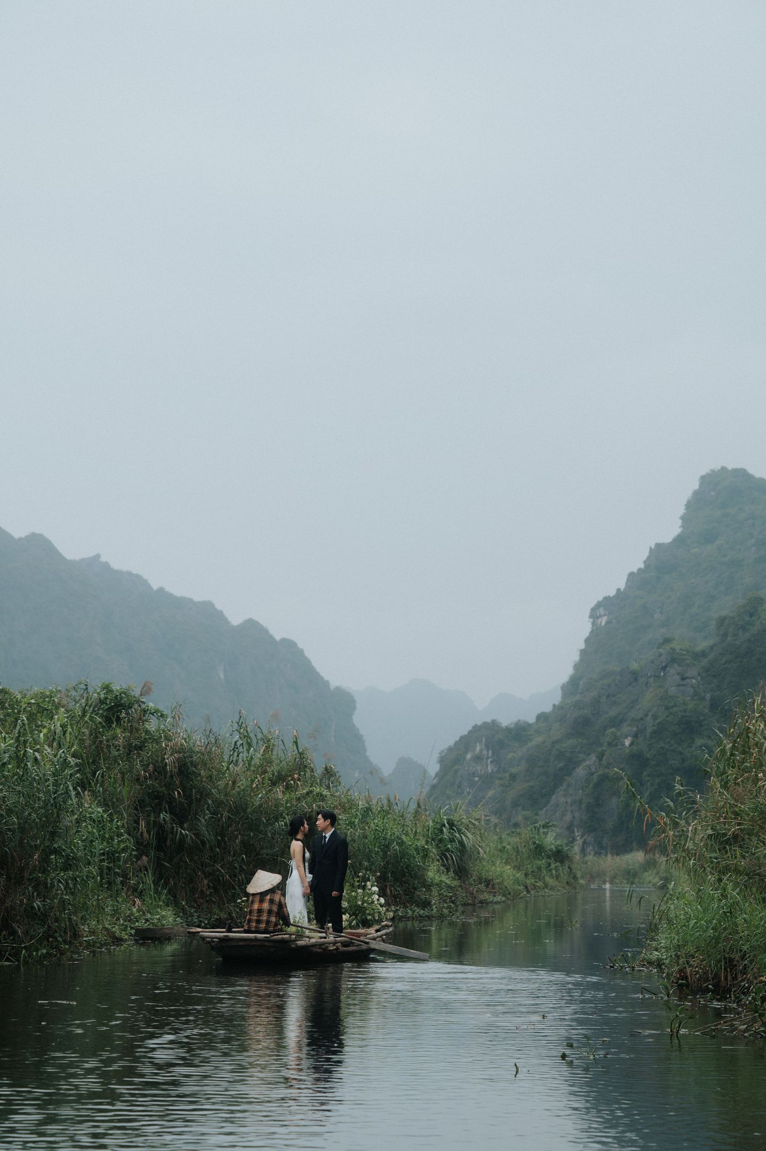 Couple sharing a romantic moment on a traditional boat in misty Ninh Binh river, surrounded by lush karst mountains.