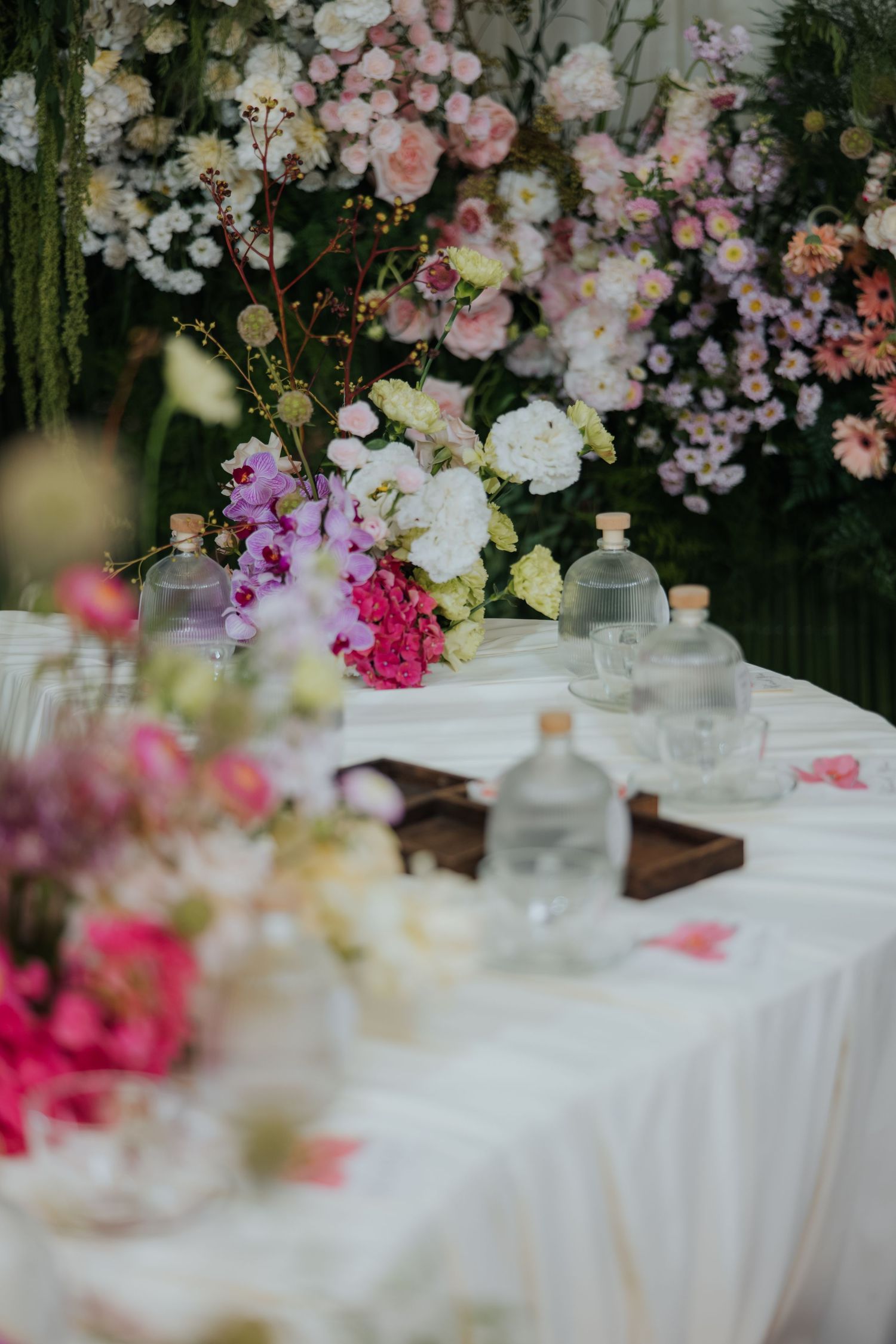 Elegant wedding table with glass bottles and lush floral arrangements in pink, white, and green tones.