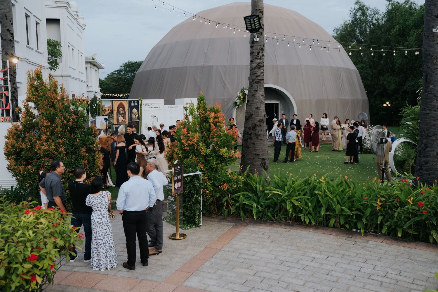 Guests mingle outside a dome venue at an elegant evening event, surrounded by lush greenery and string lights.