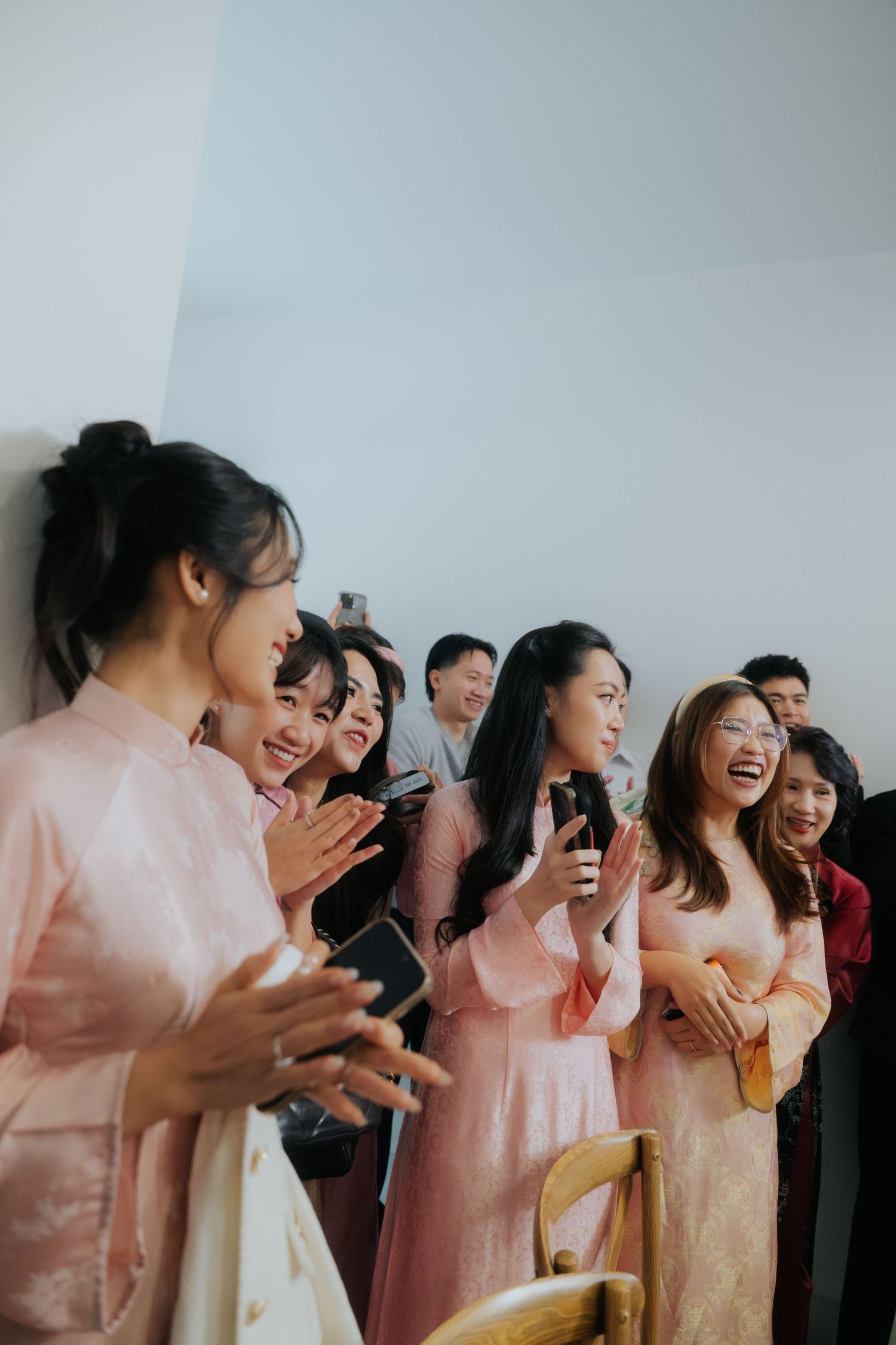 Women in pink ao dai dresses clapping and laughing joyfully at a Vietnamese wedding celebration.
