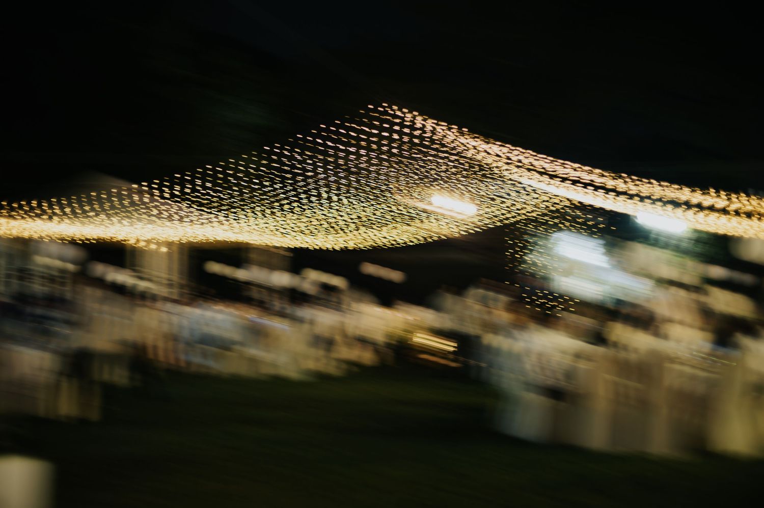 Blurred nighttime festival lights forming a glowing wave pattern against a dark sky.