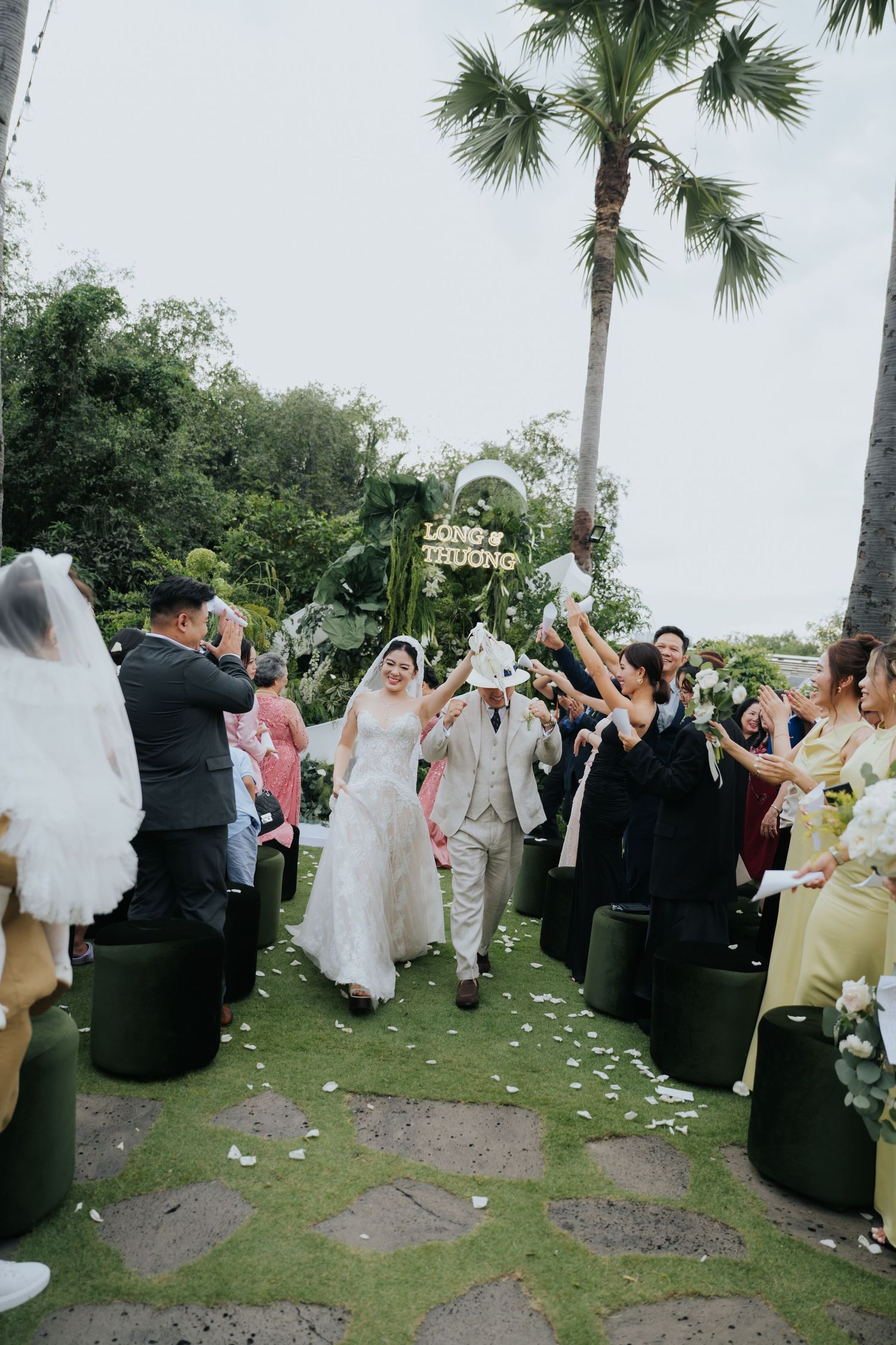 A joyful couple walks down the aisle at an outdoor garden wedding ceremony as guests celebrate around them.