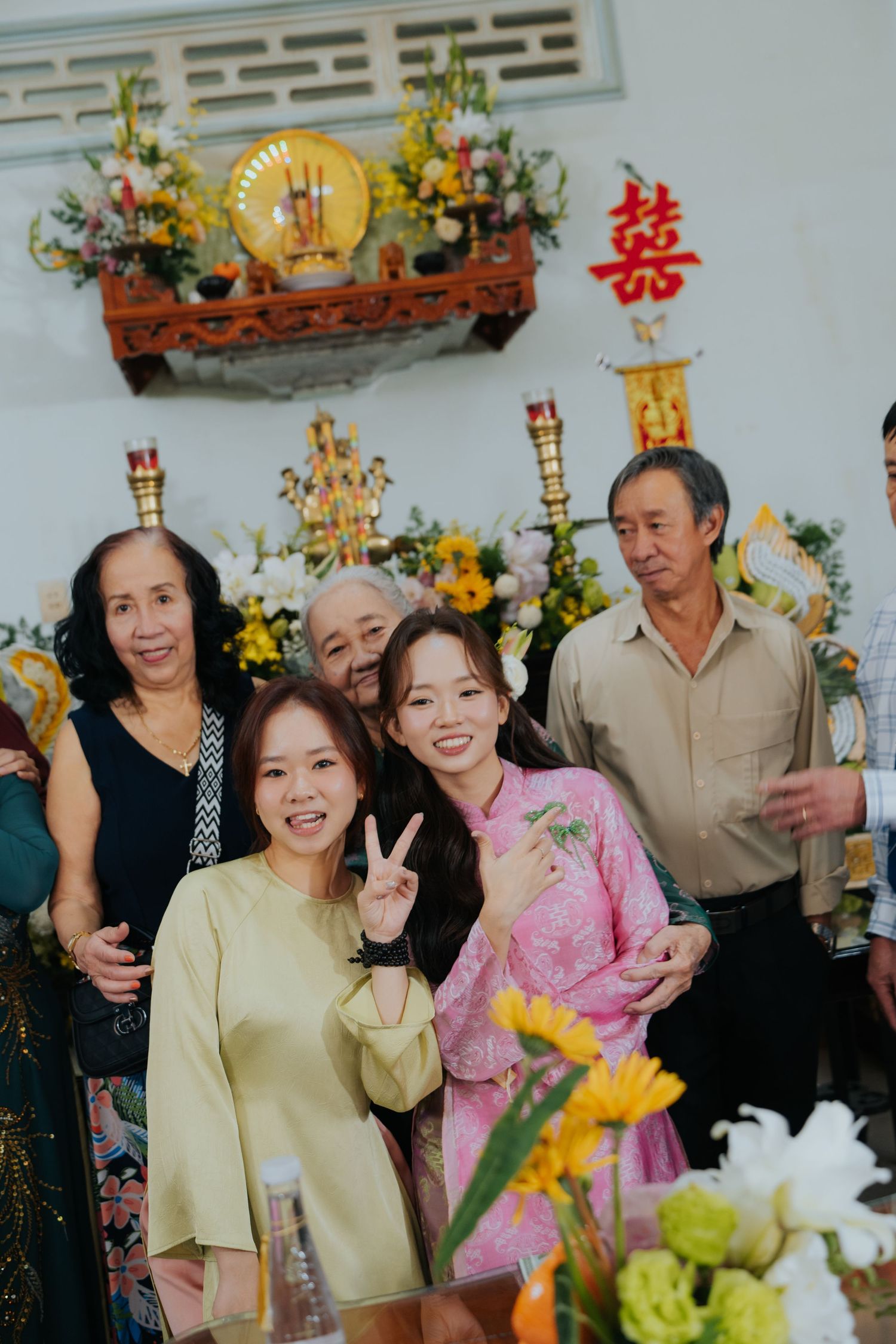 Vietnamese family posing for photo at traditional wedding ceremony with altar decorations and floral arrangements.