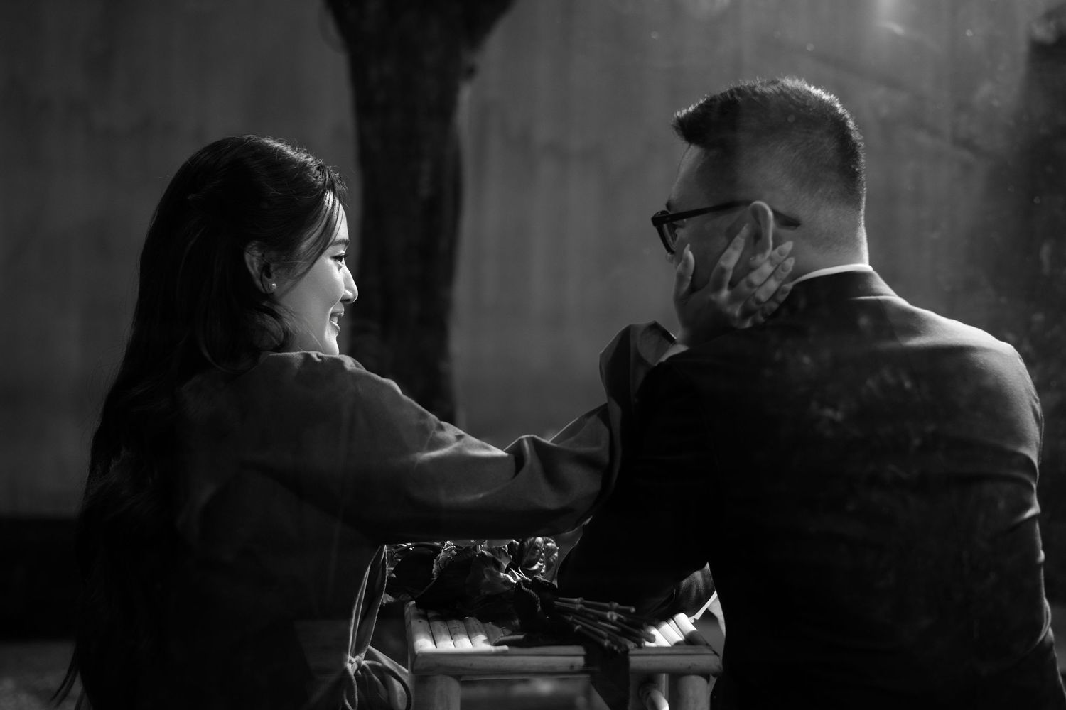 Black and white photo of a couple sharing a romantic moment, smiling and holding hands at a table.