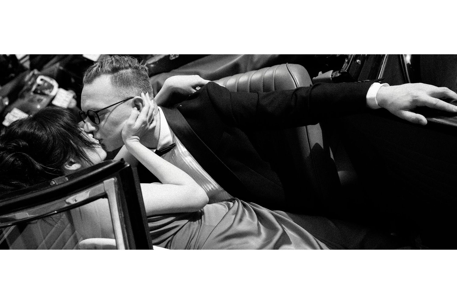 Black and white photo of a person wearing glasses leaning back in a chair at a formal event.