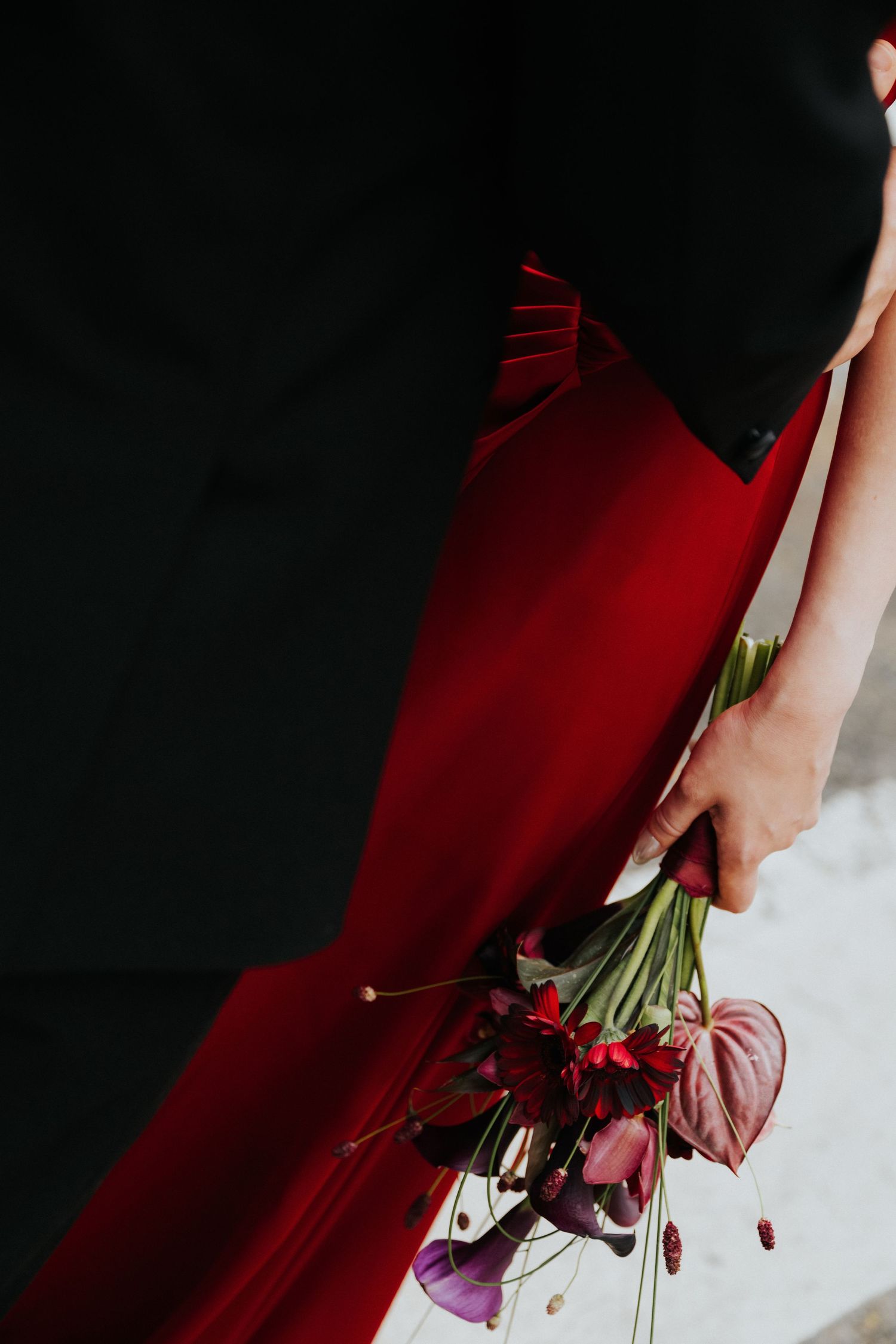 Person in red gown holding a bouquet of red and purple flowers against a dark background.