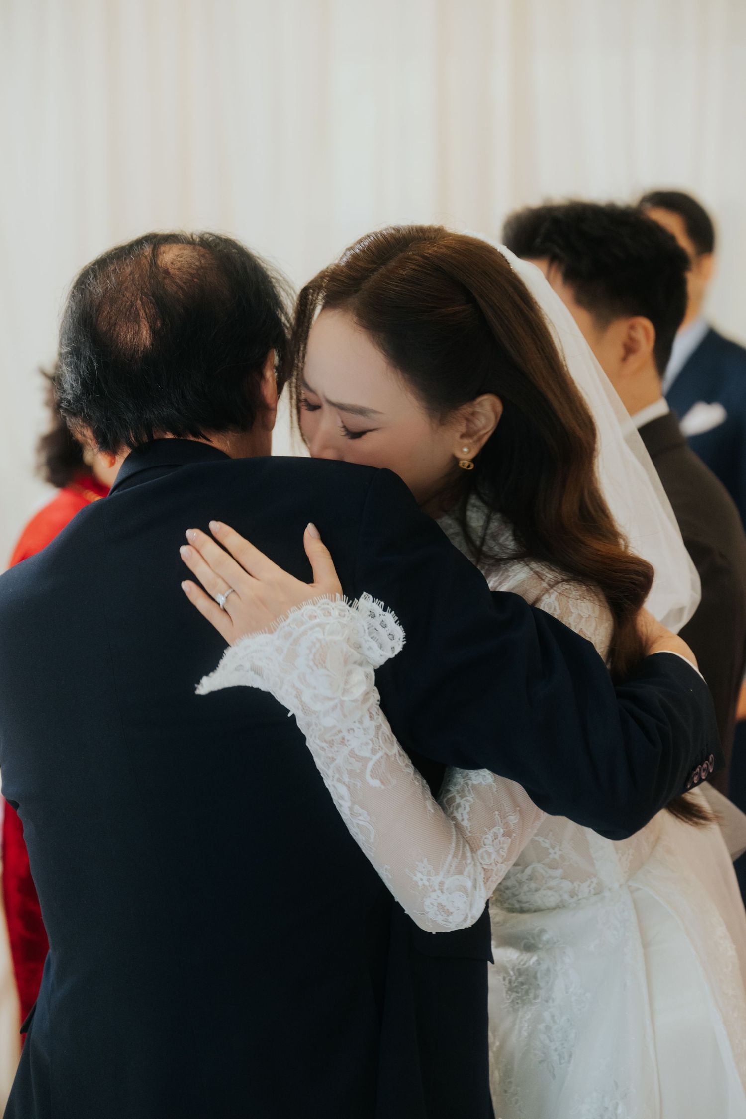 A bride in a lace wedding dress emotionally hugs a guest during her wedding reception ceremony.
