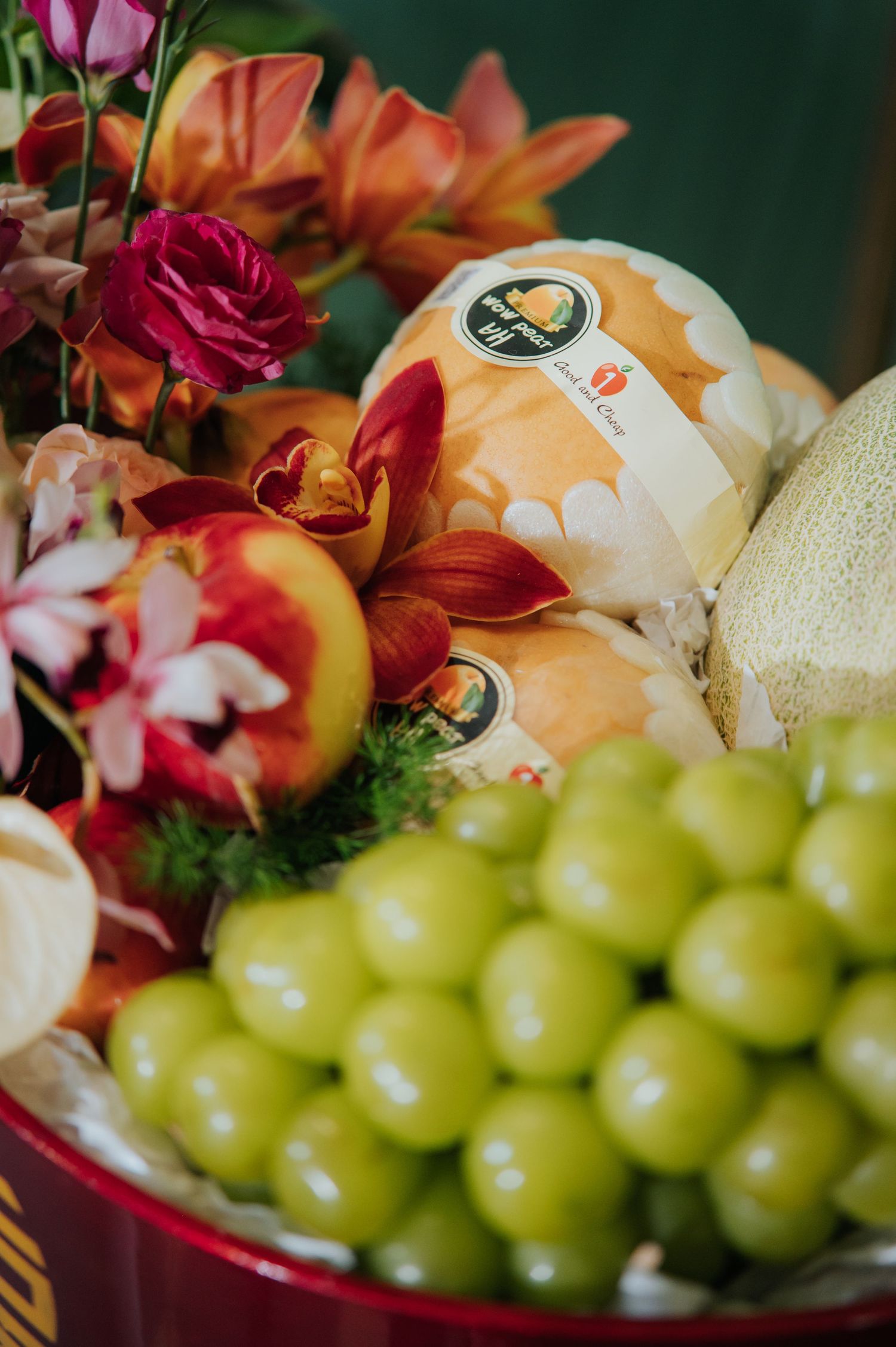 A vibrant fruit basket with green grapes, peaches, melon, and colorful flowers including roses and orchids.