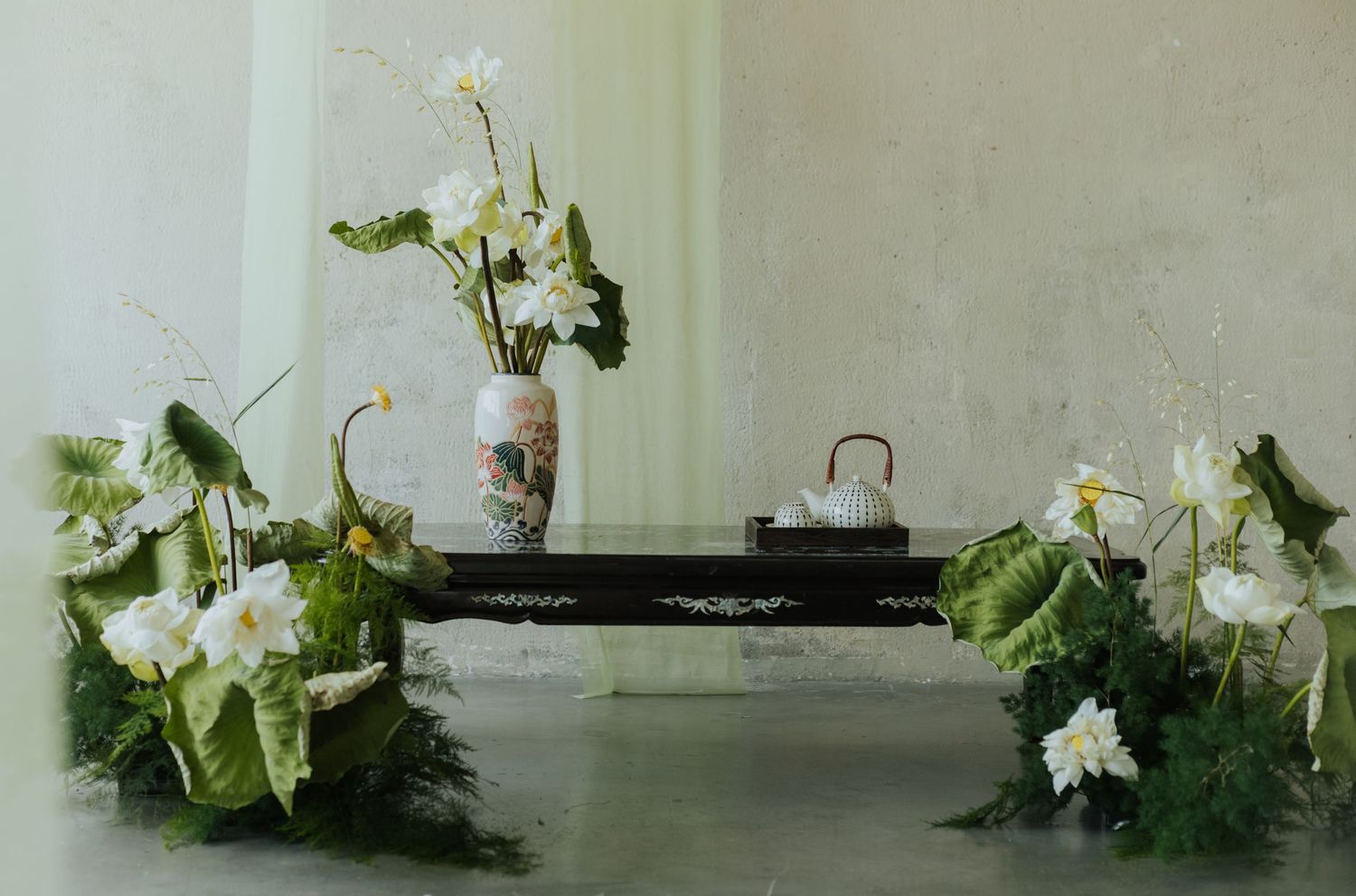 Elegant floral arrangement with white lotus flowers, green leaves, and a decorative vase on a dark wooden table.