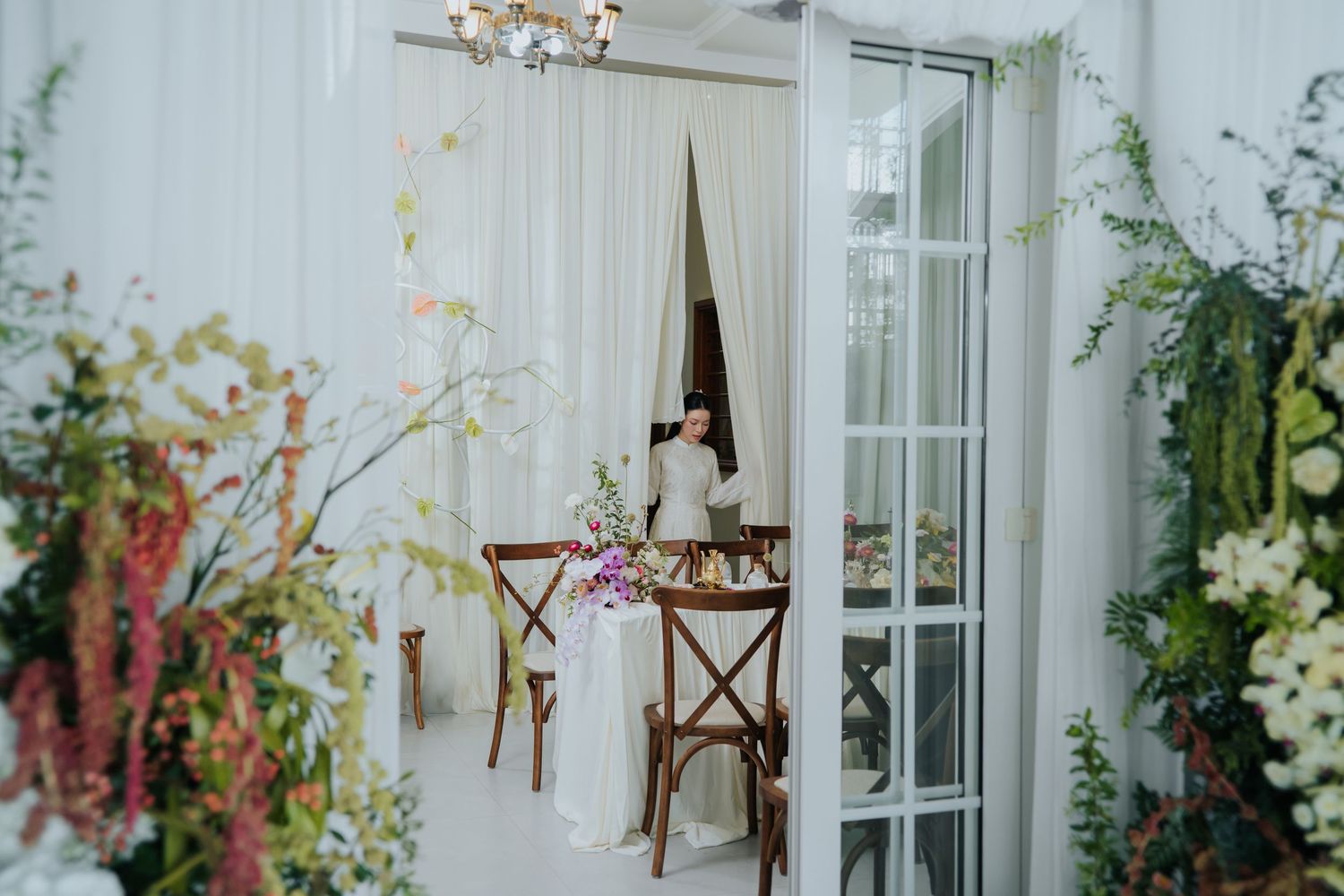 Elegant wedding reception setup with floral arrangements, sheer curtains, and a decorated table in a white venue.