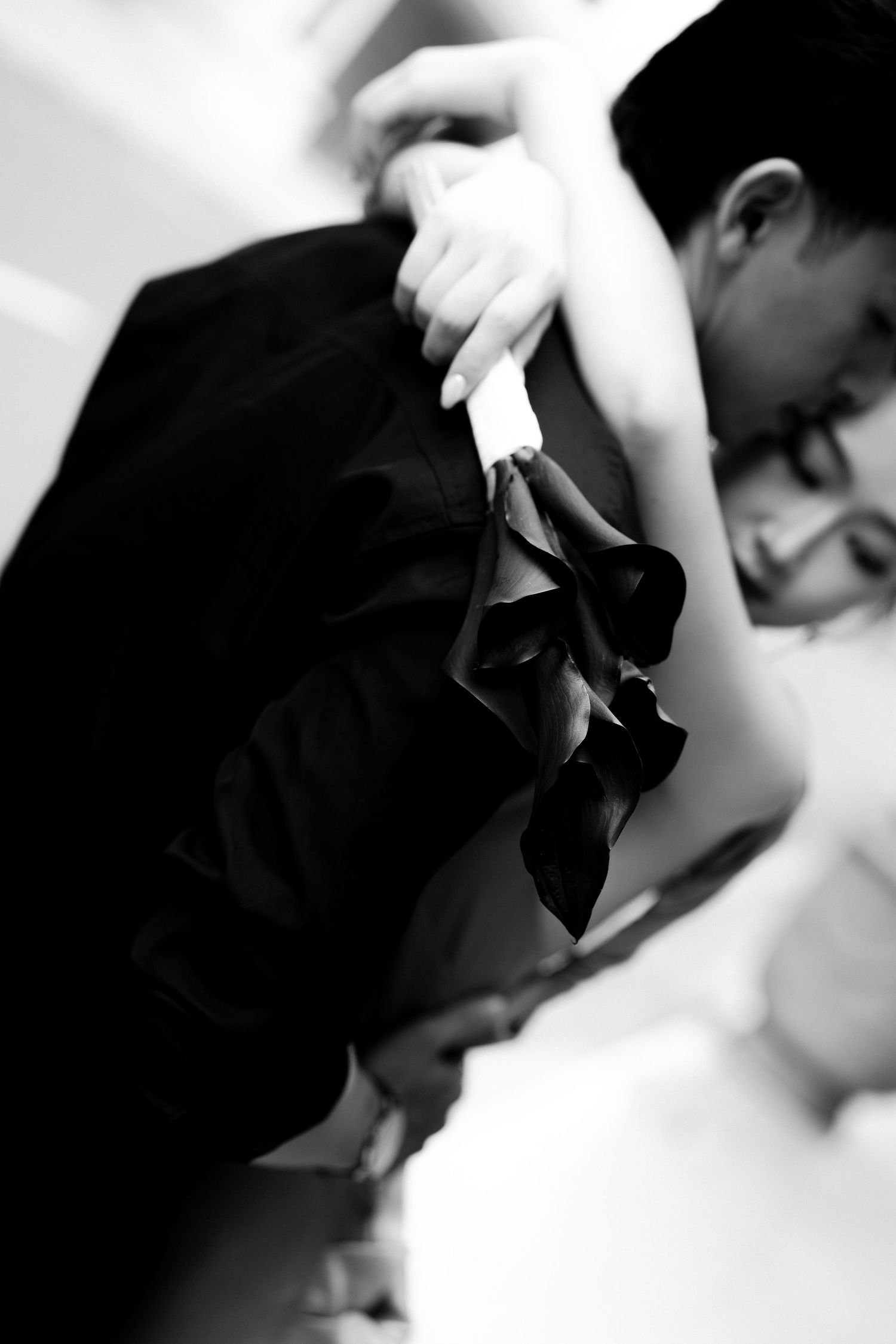Black and white photo of a couple sharing a romantic kiss, bride holding dark calla lilies bouquet at their wedding.