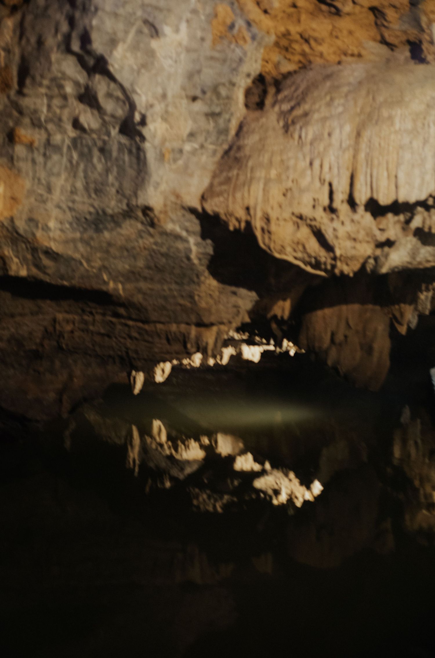 Dark cave interior with still water reflecting stalactites and limestone formations in dramatic underground setting.